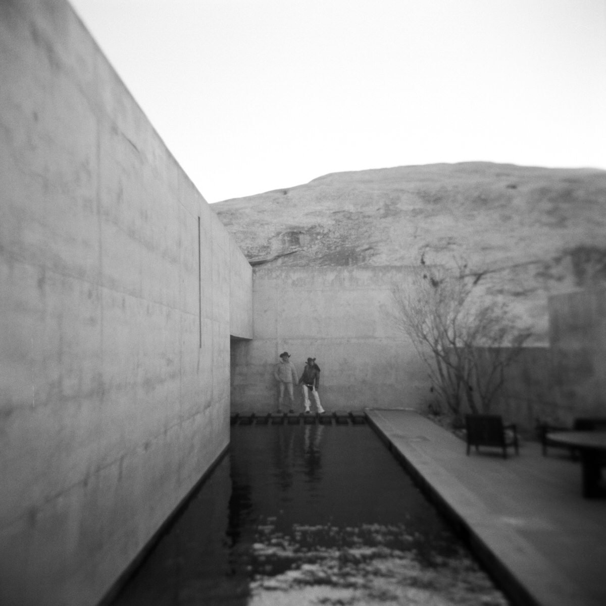 black and white film couple holding hands surrounded by concrete walls and water at amangiri