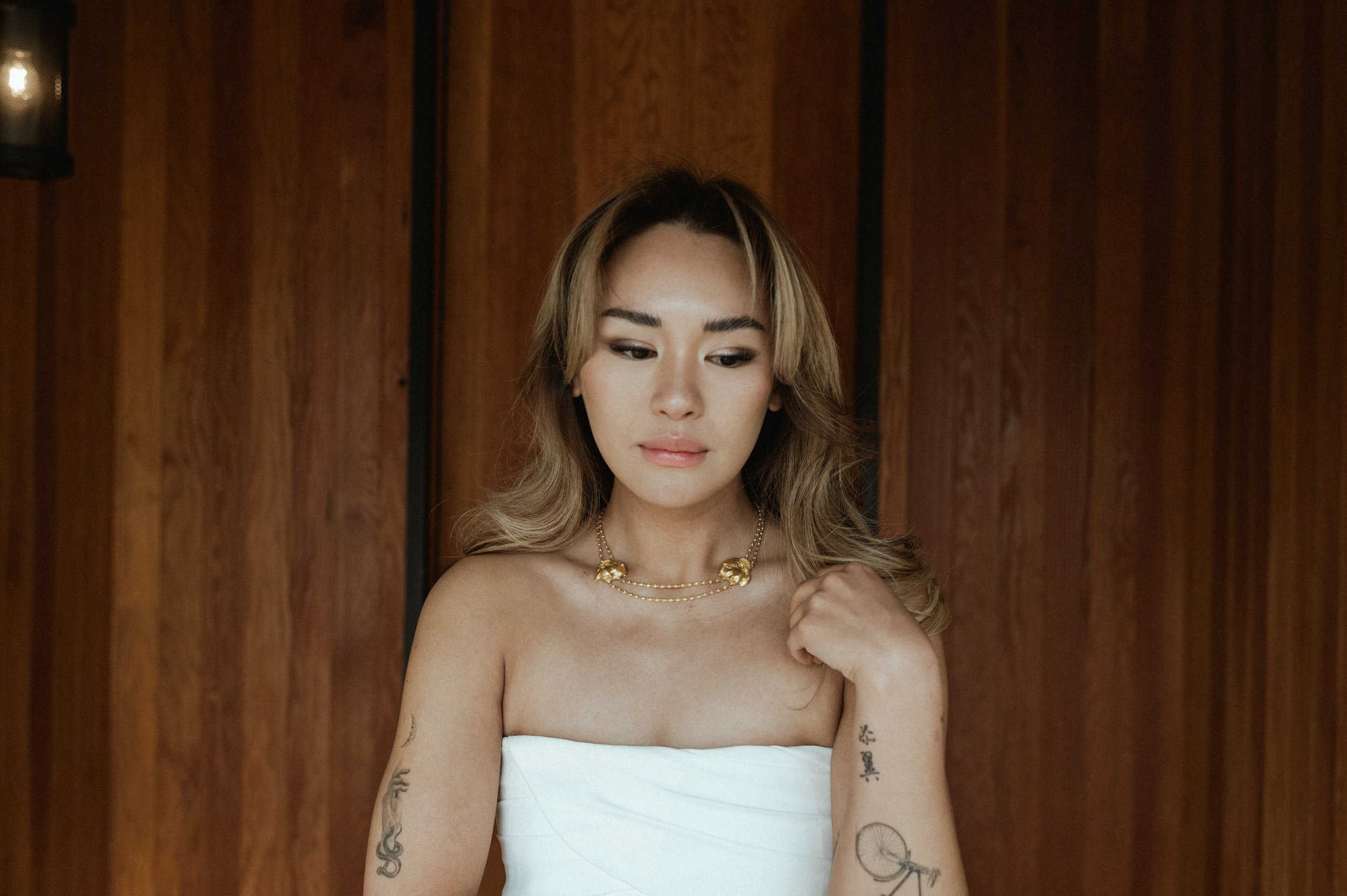 asian woman of color in white dress wearing custom gold necklace in front of wooden doors at amangiri camp sarika