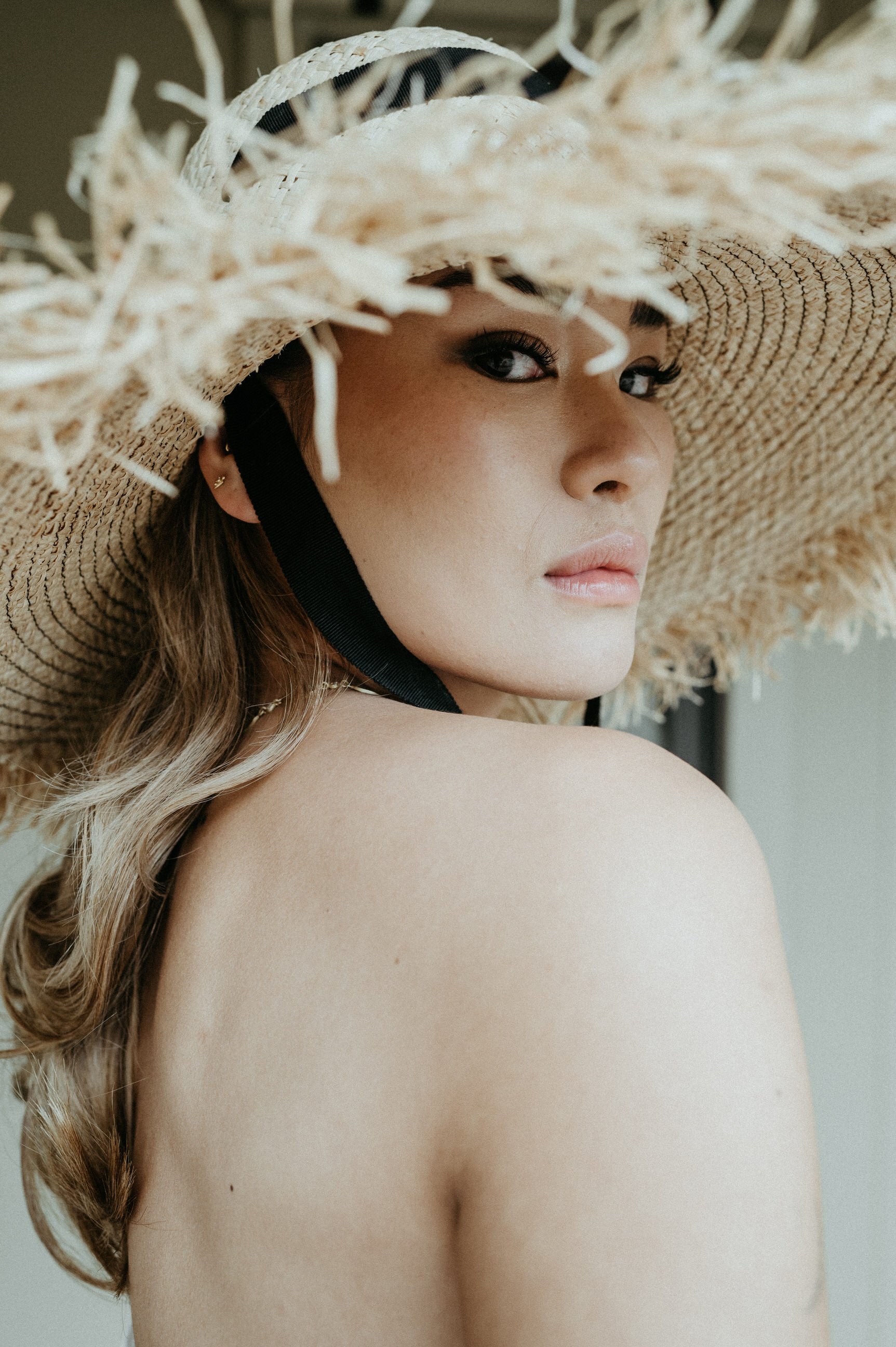 asian woman of color with bold winged eyeliner in straw hat with black ribbon looking at camera