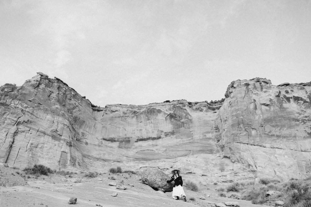 black and white photo of woman in asymmetrical dress with oversized black blazer with desert mesa backdrop 