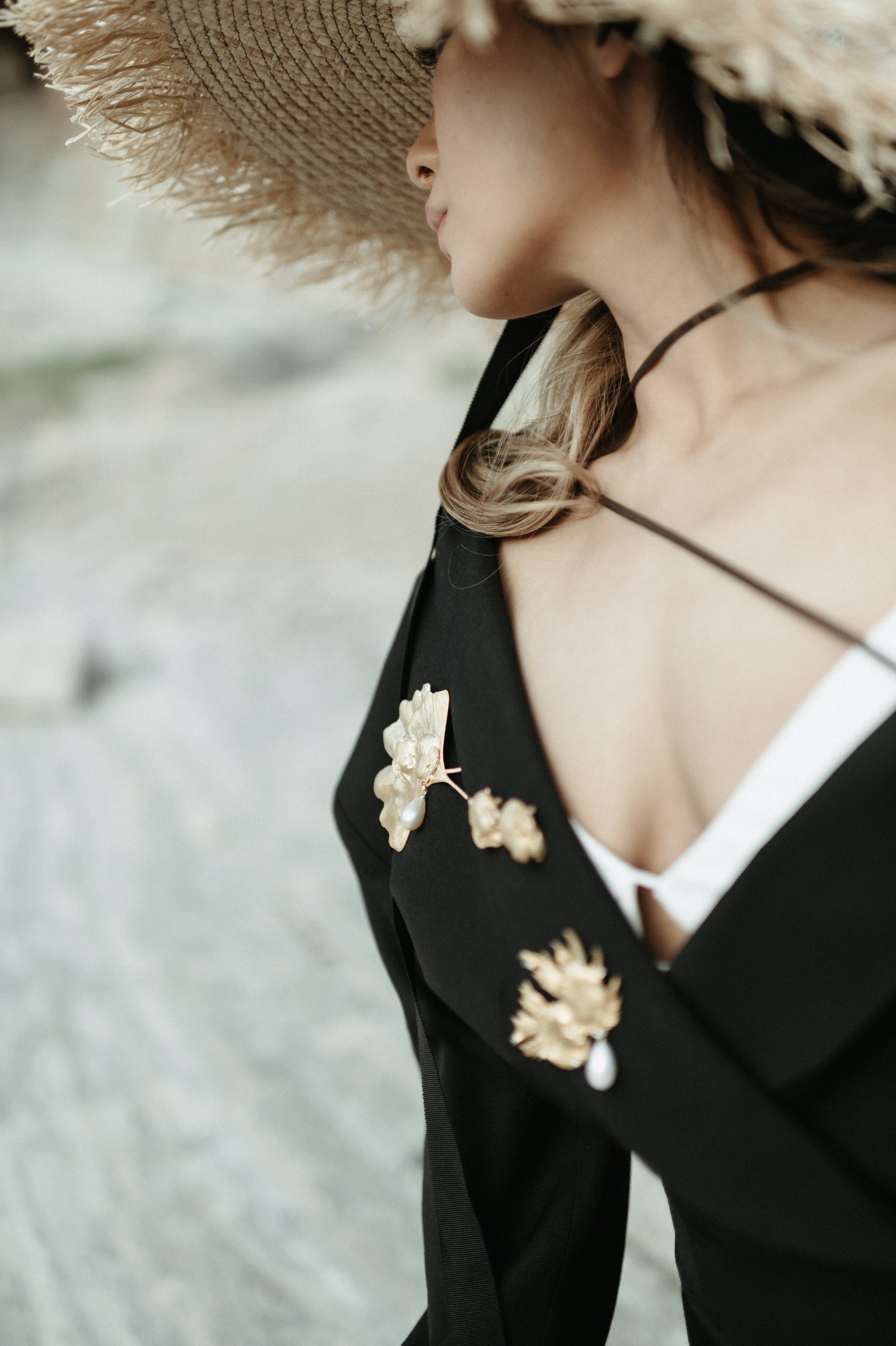 black and white photo of woman in white dress with oversized black blazer wearing custom gold jewelry broaches in large straw hat desert backdrop