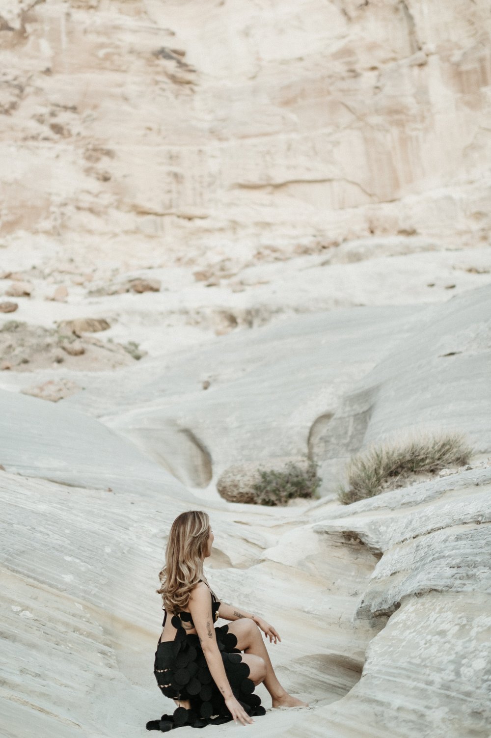 woman in desert crouched down hand on rock face tilted upward toward desert mesa black circle cutout dress