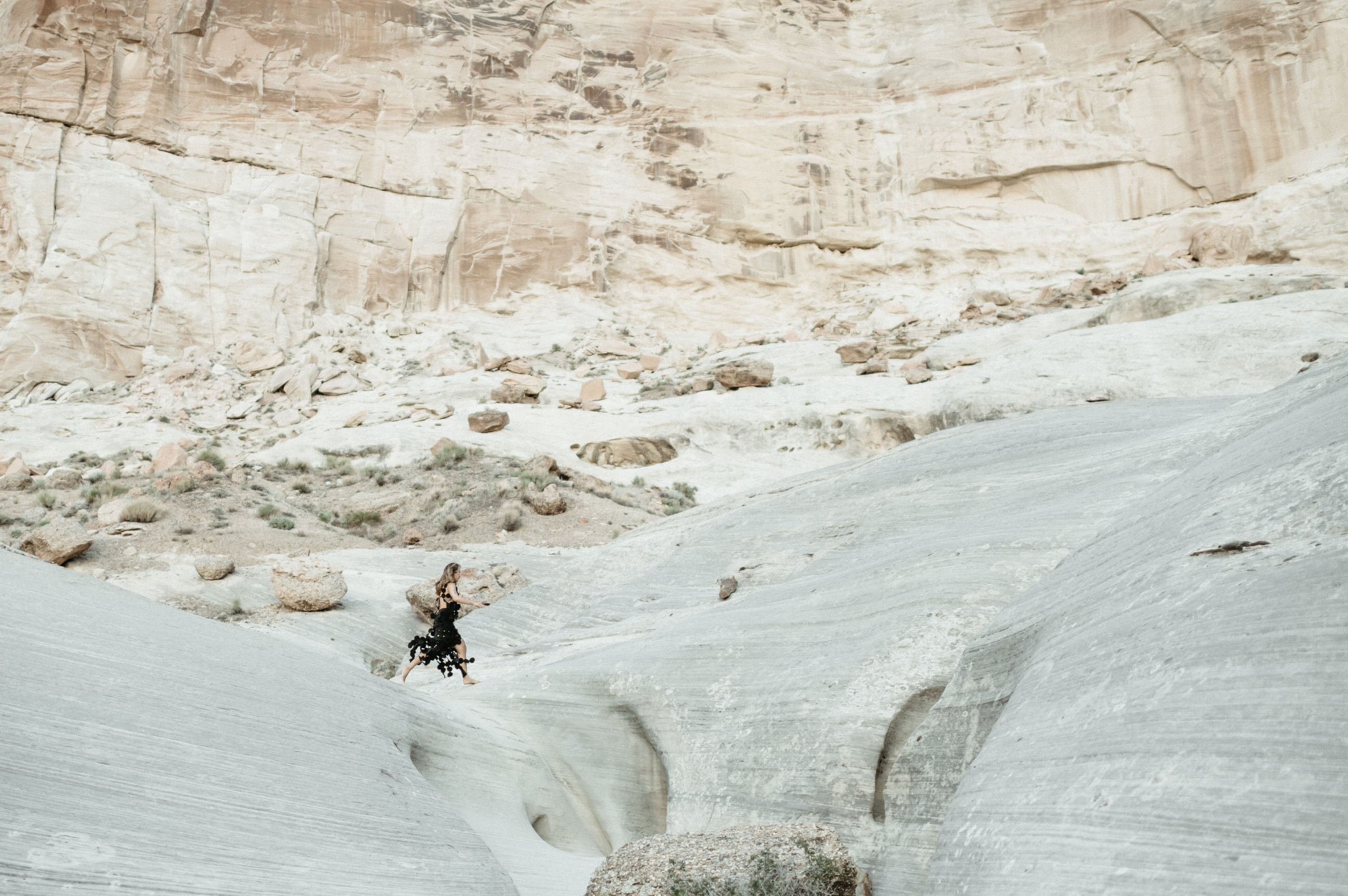woman in desert leaping across slot canyon opening with large cliff background black circle cutout dress