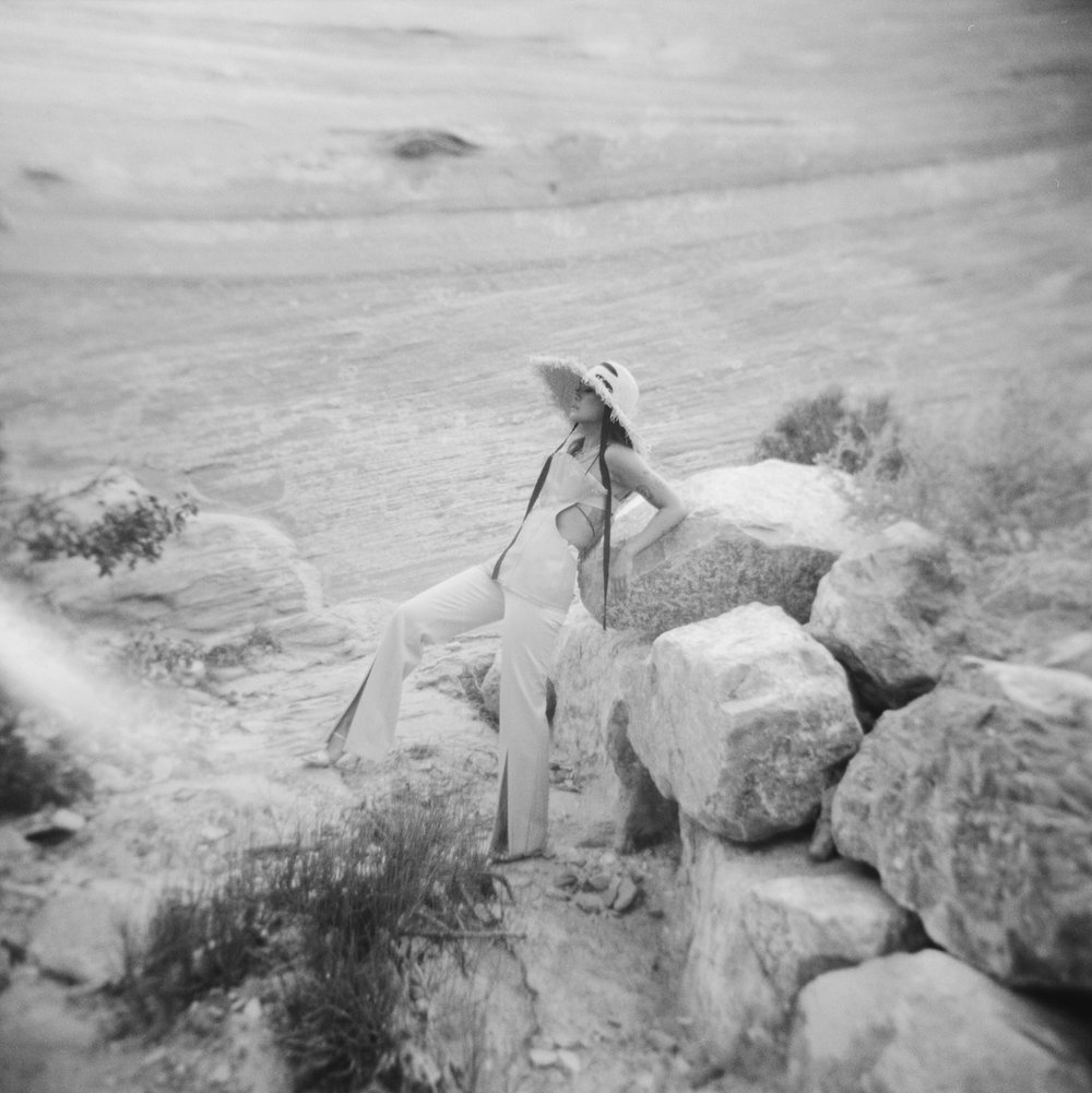 black and white holga square photo of woman in editorial straw hat and top leaning arms back on rock in desert at amangiri resort