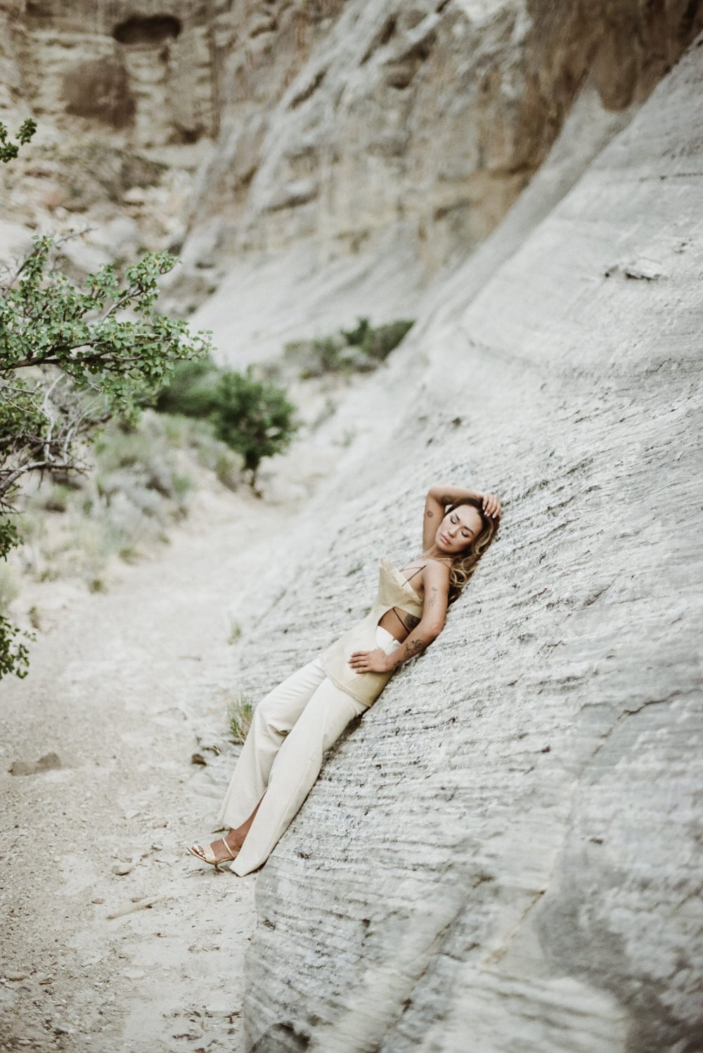 asian woman of color in straw editorial hat and top with cutouts black ribbon leaning body on rock in desert