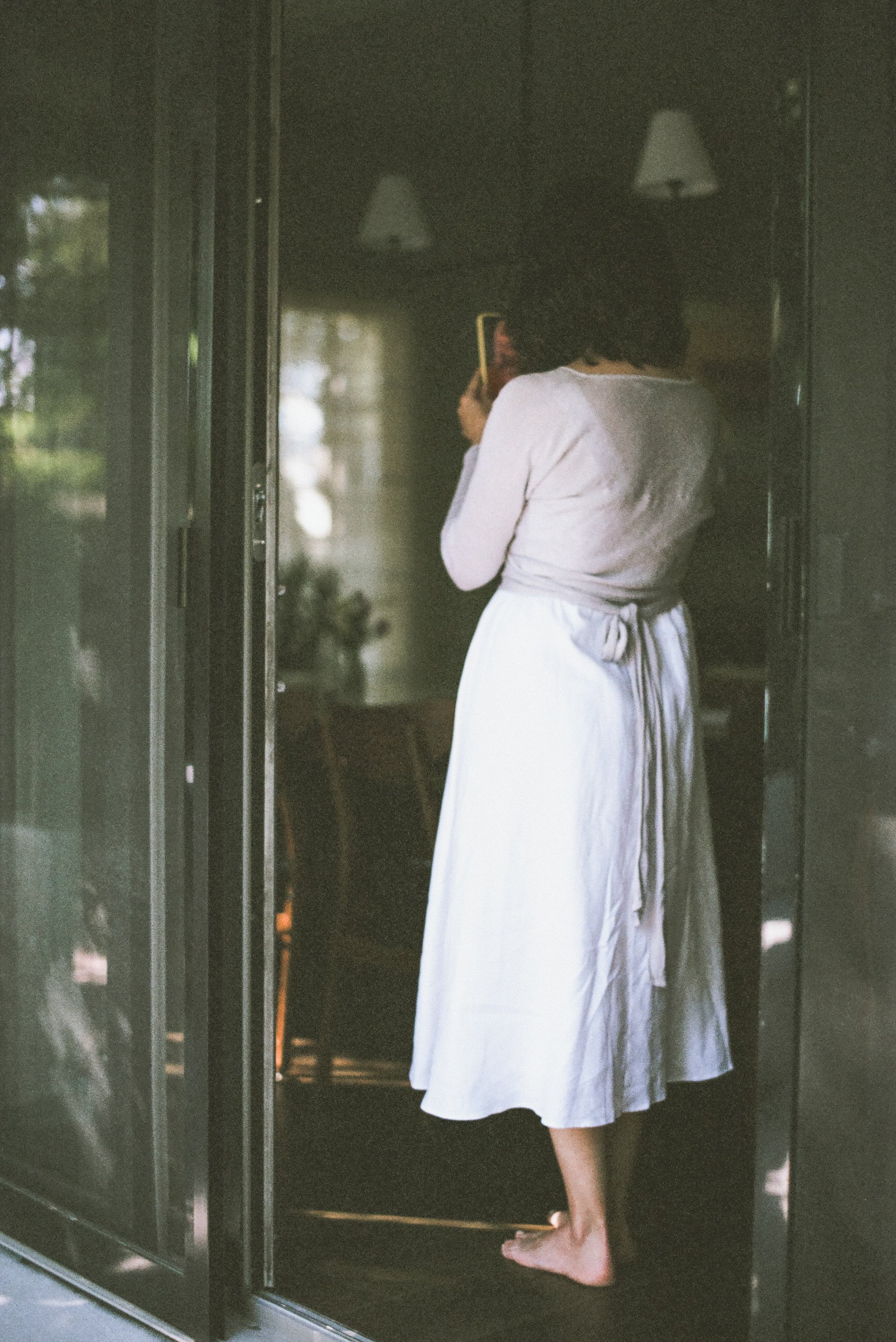 film photo of bride standing in doorway in white dress gray cardigan