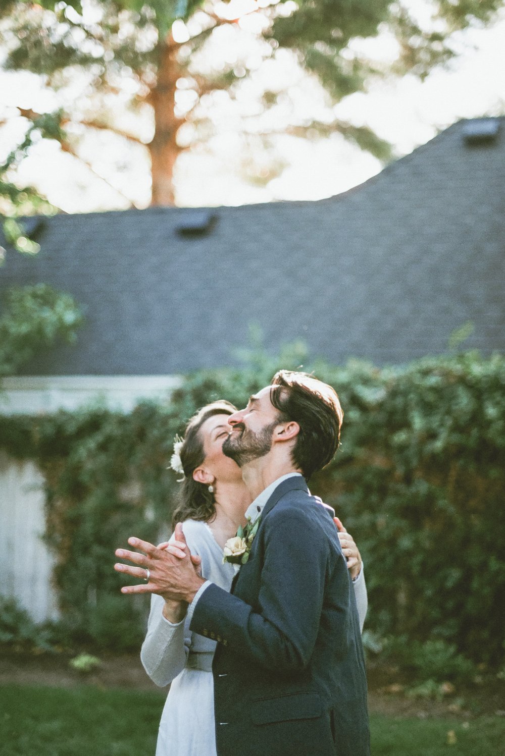 film photo bride and groom first dance bride kissing groom on cheeck groom eyes closed face tilted upward with sunlight on his hair and greenery in background