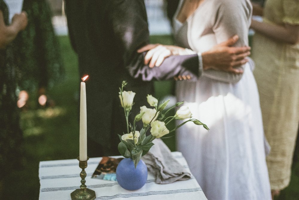 single candle blue vase with yellow tulips striped linen on small table bride and grooms arms and hands touching in background