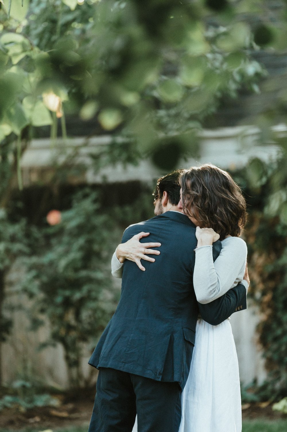 bride and groom embrace in greenery after first dance in backyard