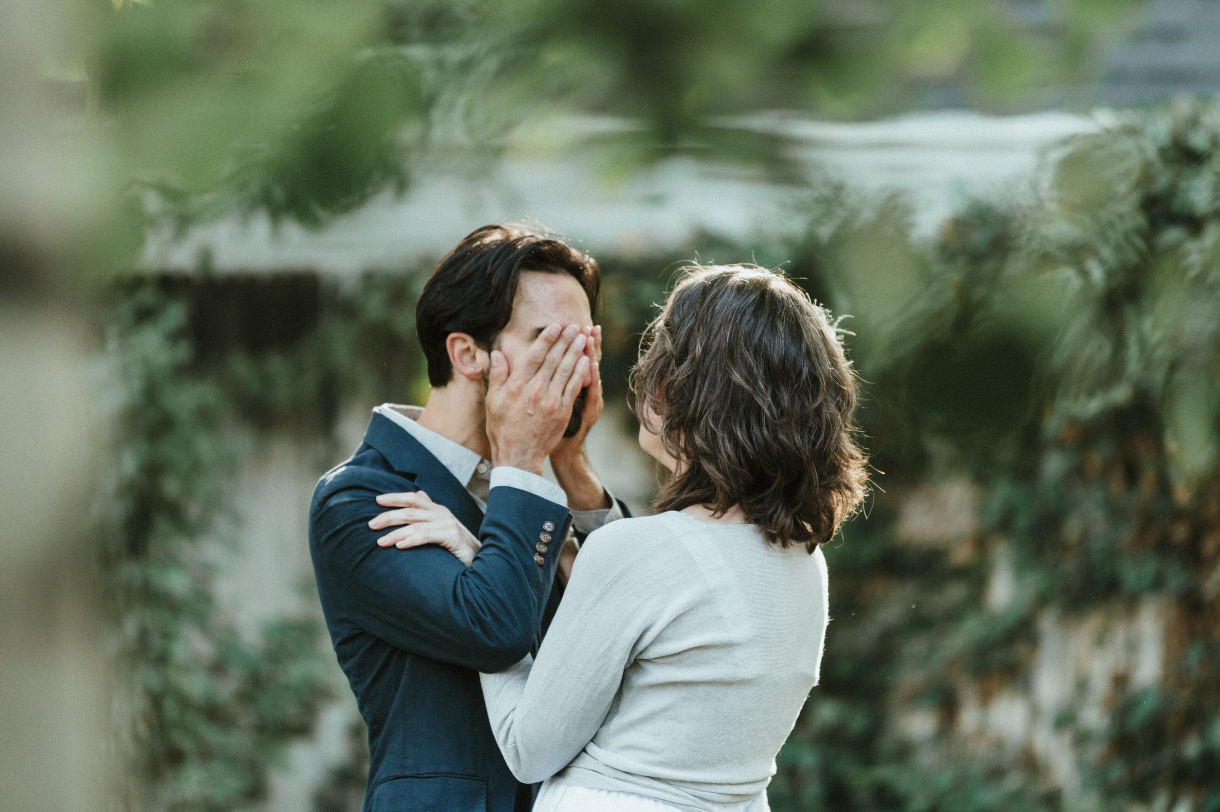 groom wiping tears away from eyes with bride holding onto his shoulders smiling