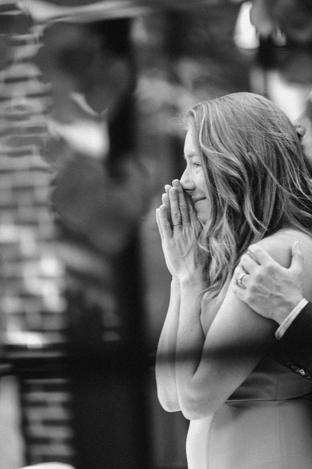 emotive photo woman watching bride dance with groom with her hands up to her face smiling
