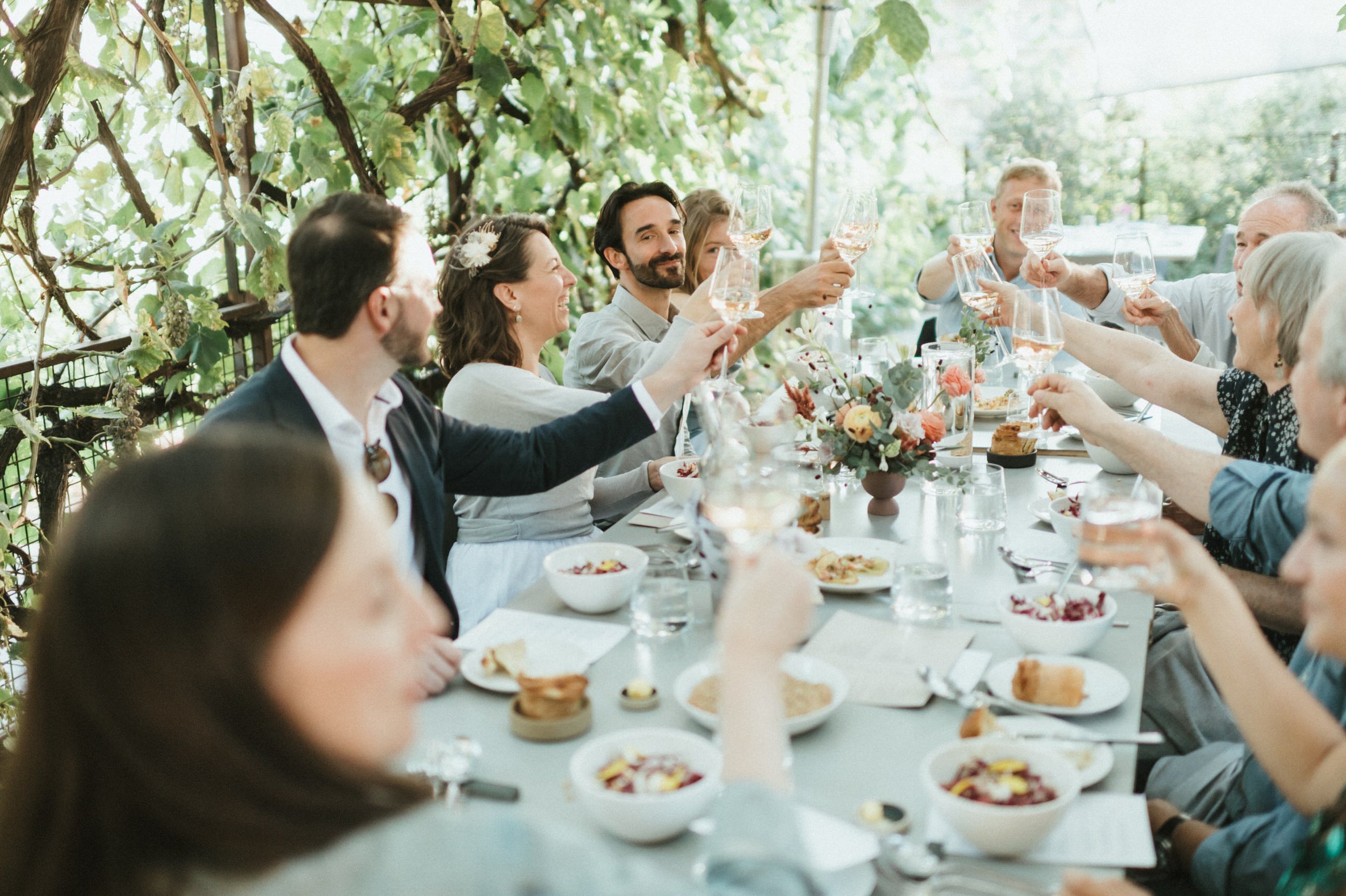 wedding party at table with colorful florals and backlighting doing cheers with wine glasses