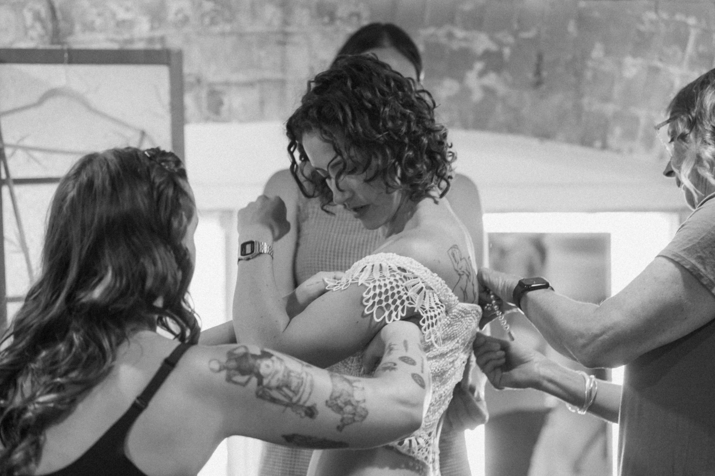 bride with mom and sisters helping her into her dress