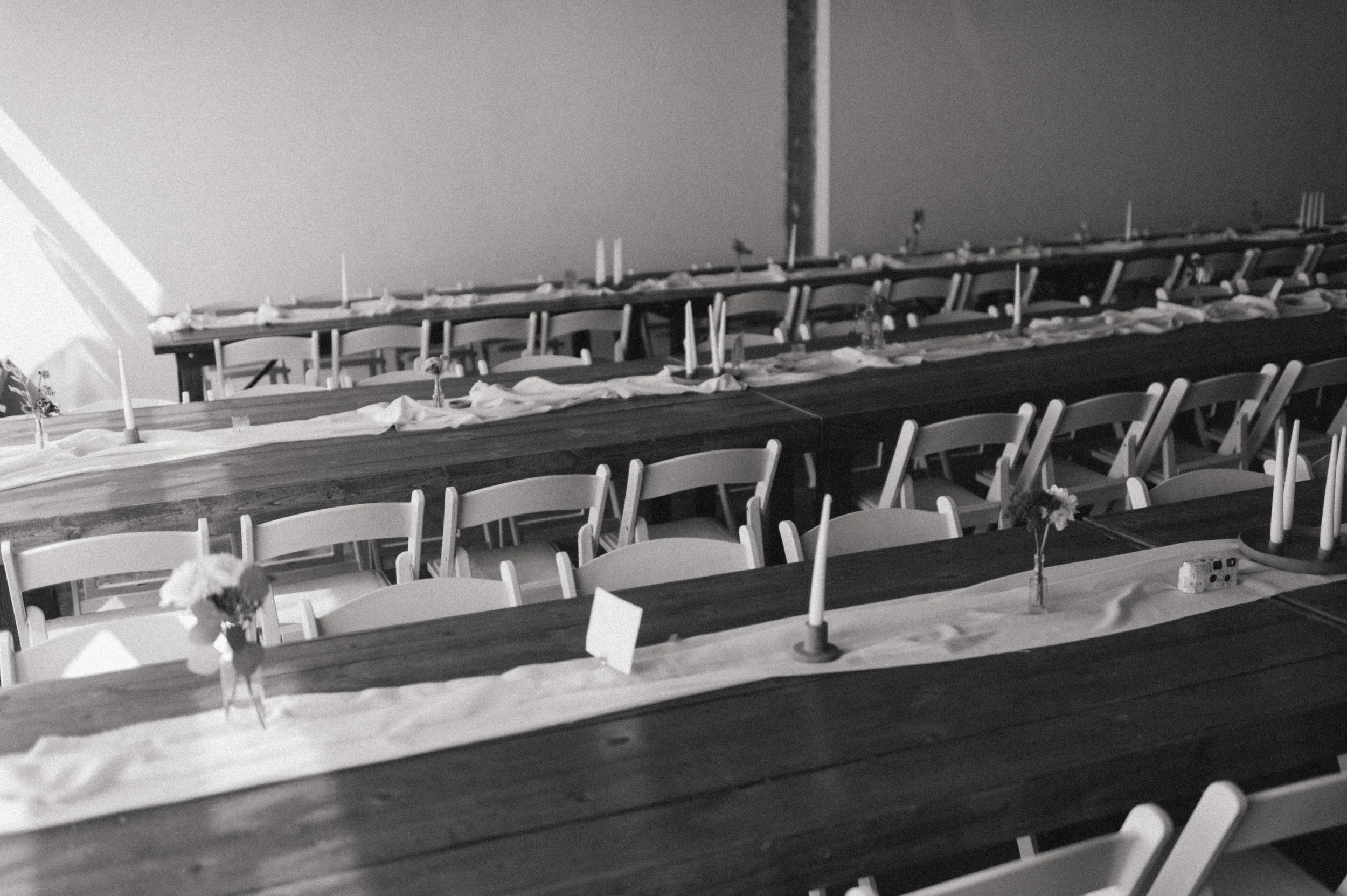 black and white photo of wooden tables linen table runners with candlesticks and flowers with window lighting