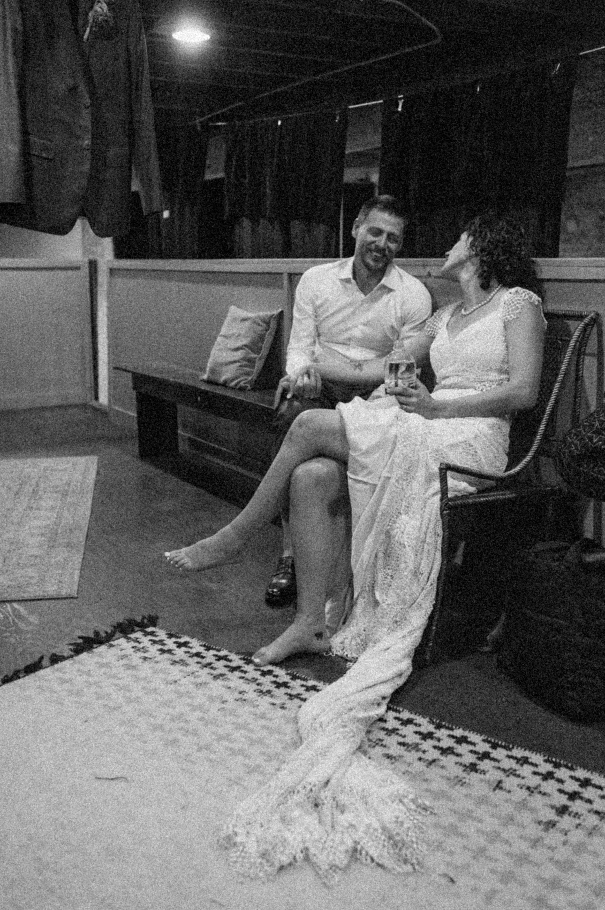 black and white photo of bride and groom sitting on couch with shoes off after ceremony