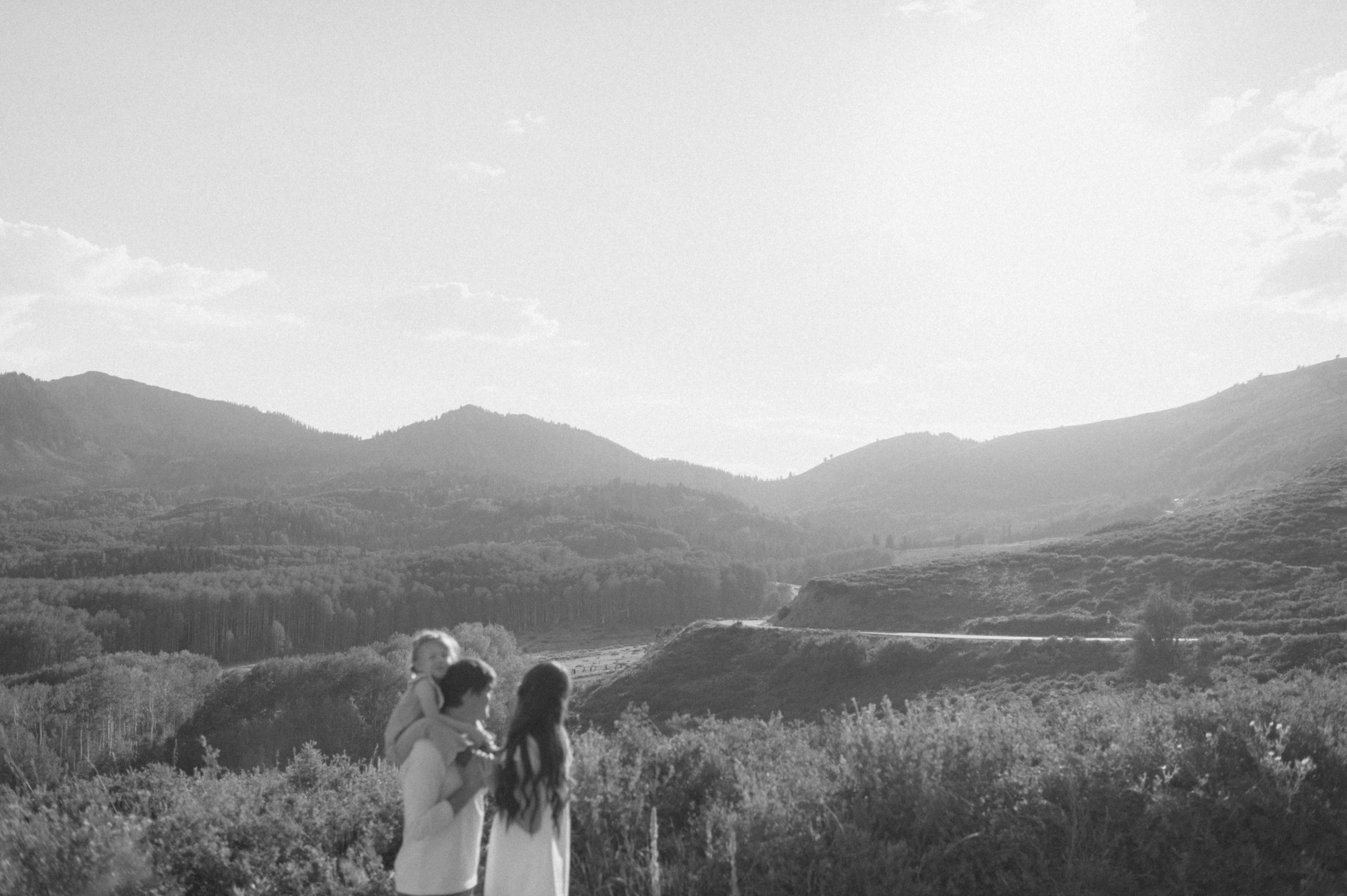 black and white photo family of three with toddler on dads shoulder and windy mountain road and Utah mountain background