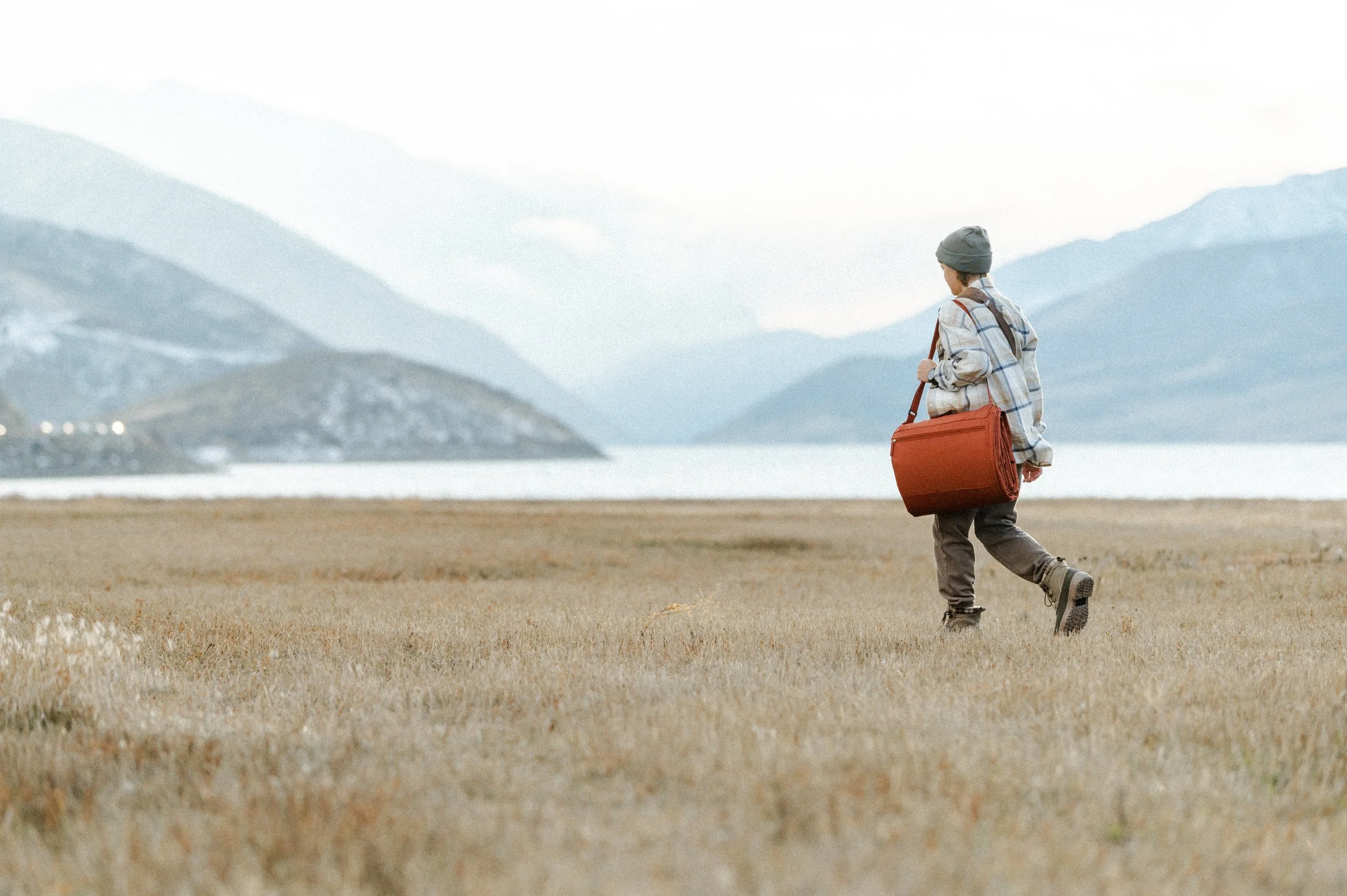 Small business product photographer capturing lifestyle shot of picnic blanket bag at golden hour by mountain lake