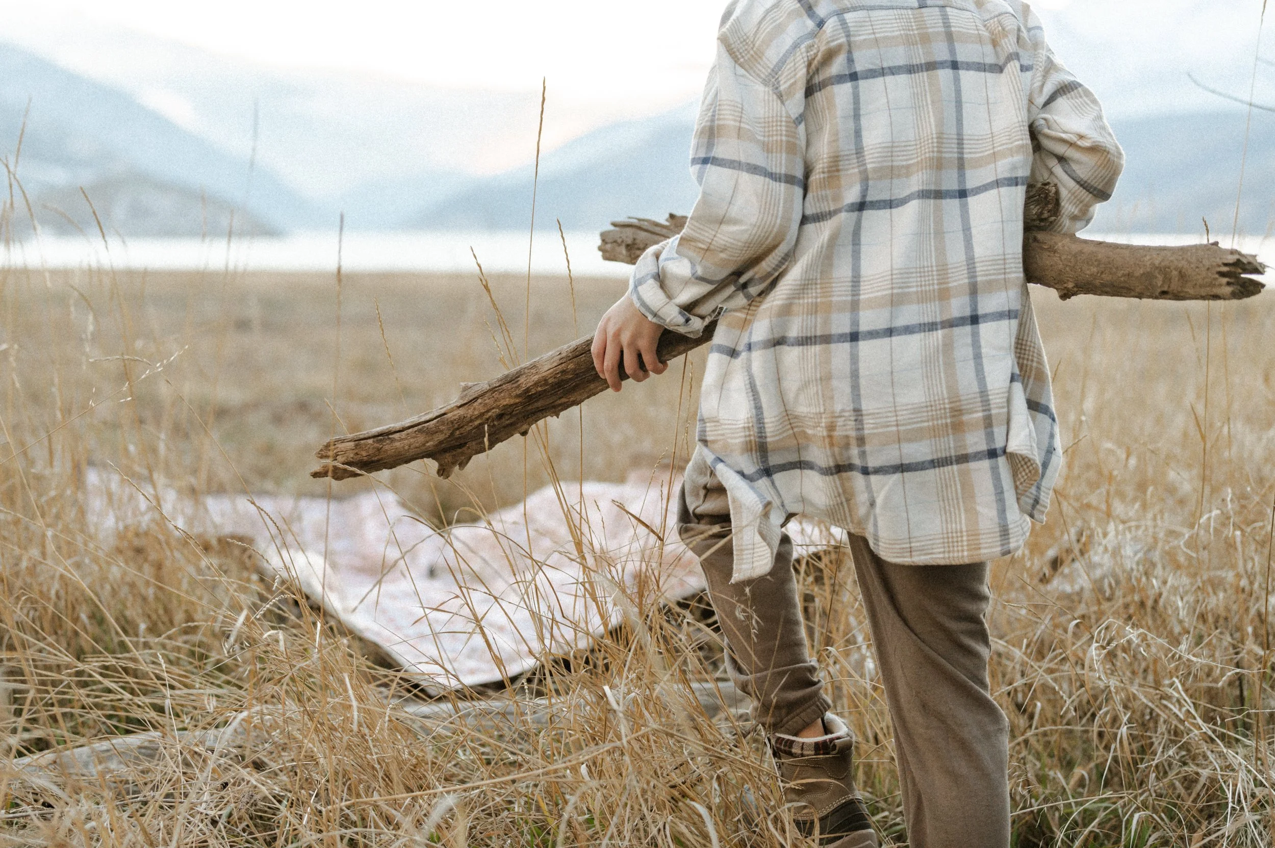 Kid stacking firewood next to camping picnic blanket, product photographer near me style shoot