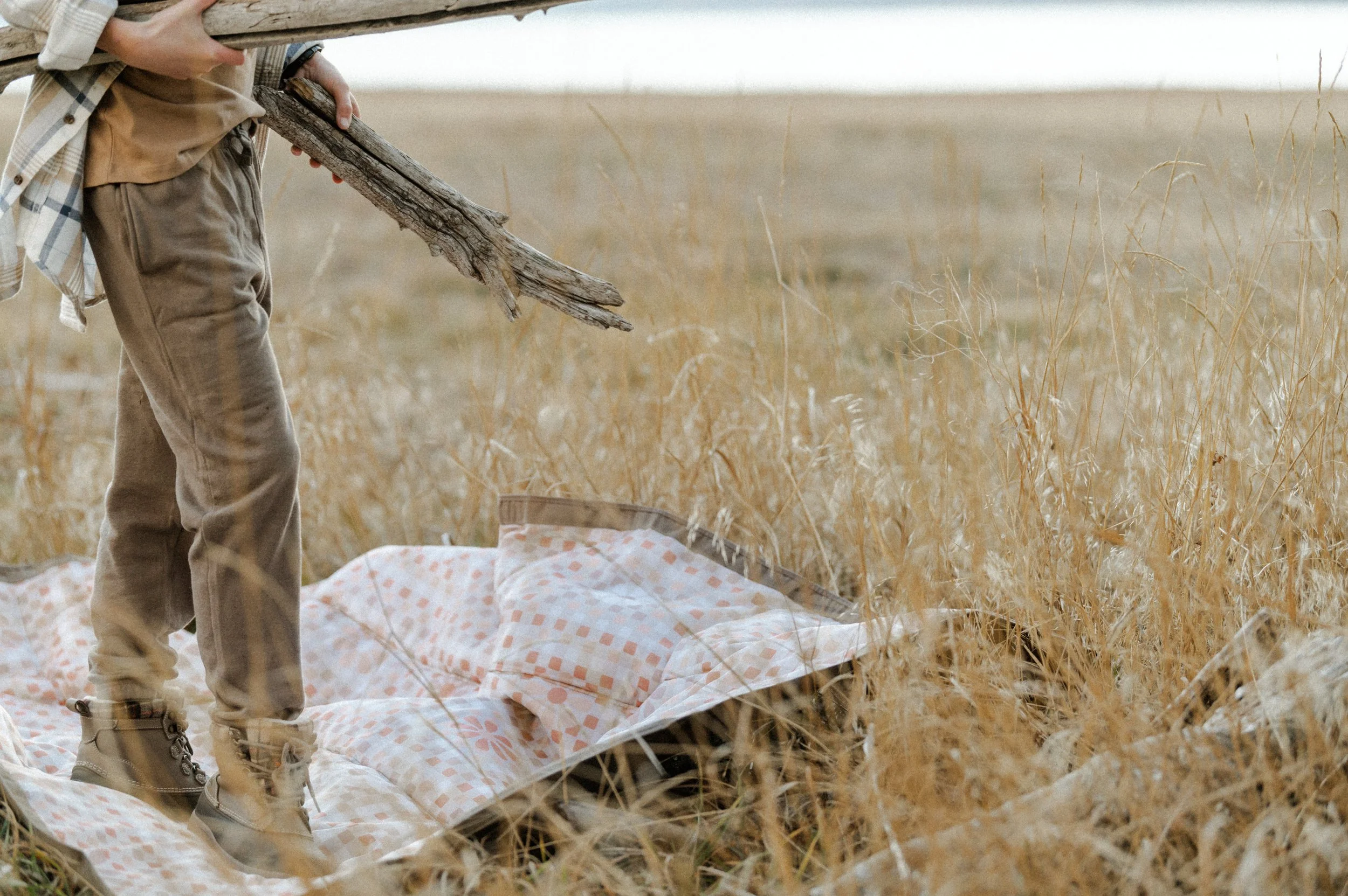 Kid stacking firewood next to camping picnic blanket, product photographer near me style shoot