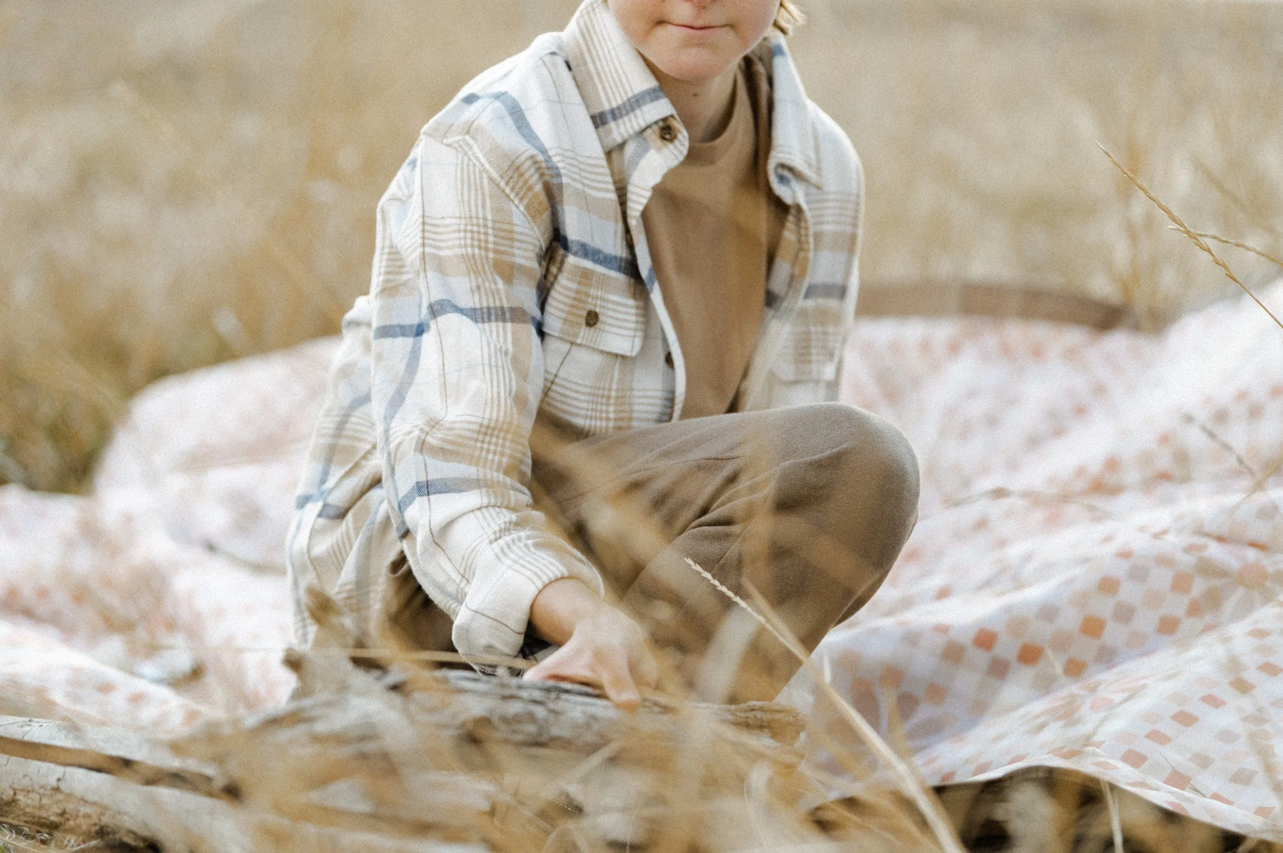 Kid stacking firewood next to camping picnic blanket, product photographer near me style shoot