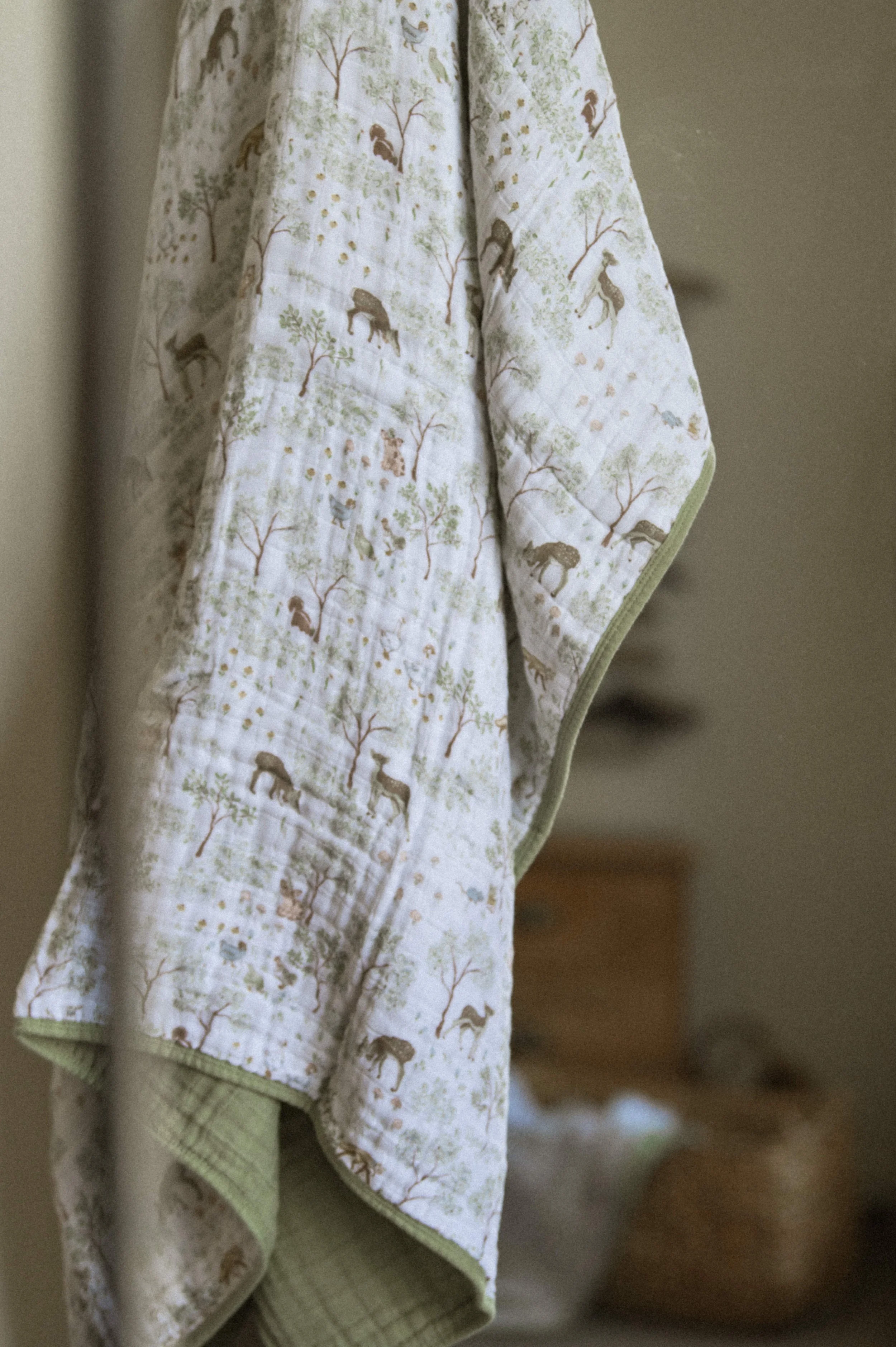 Lifestyle product photography of organic cotton quilt in woven basket, boho nursery stylingBest product photographer flat lay of organic cotton muslin quilts with forest animal print