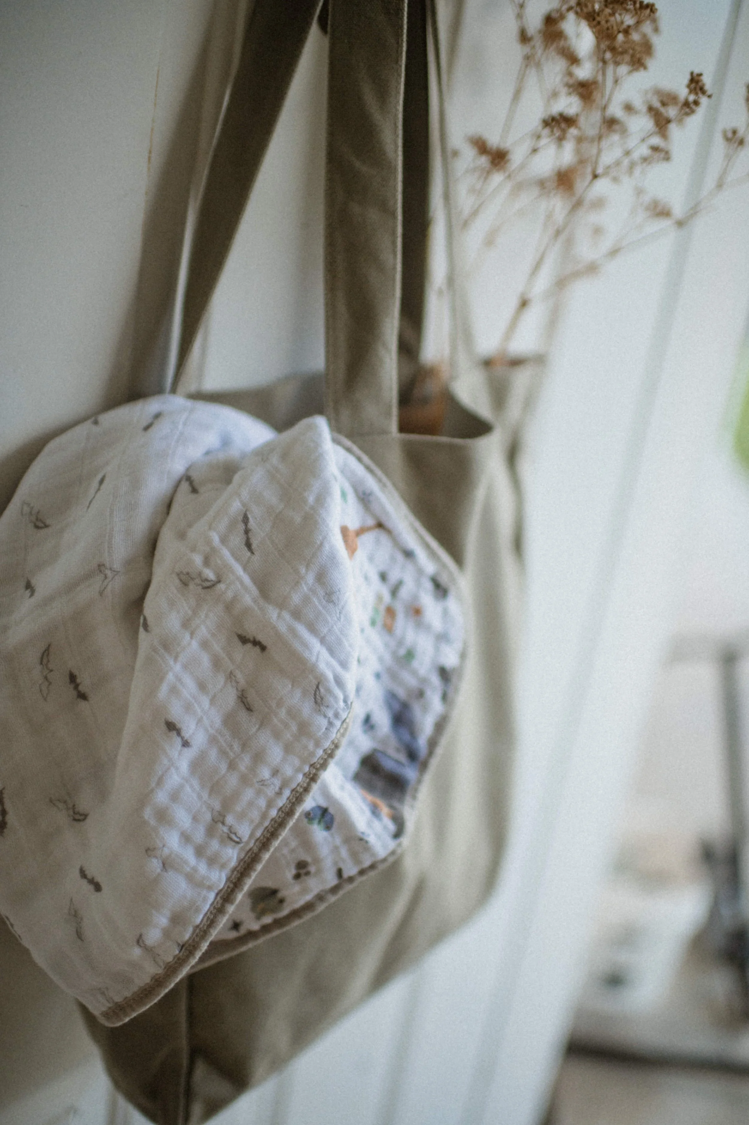 minimalist white blanket with small bats organic cotton blanket in green tote and dried florals hanging on door