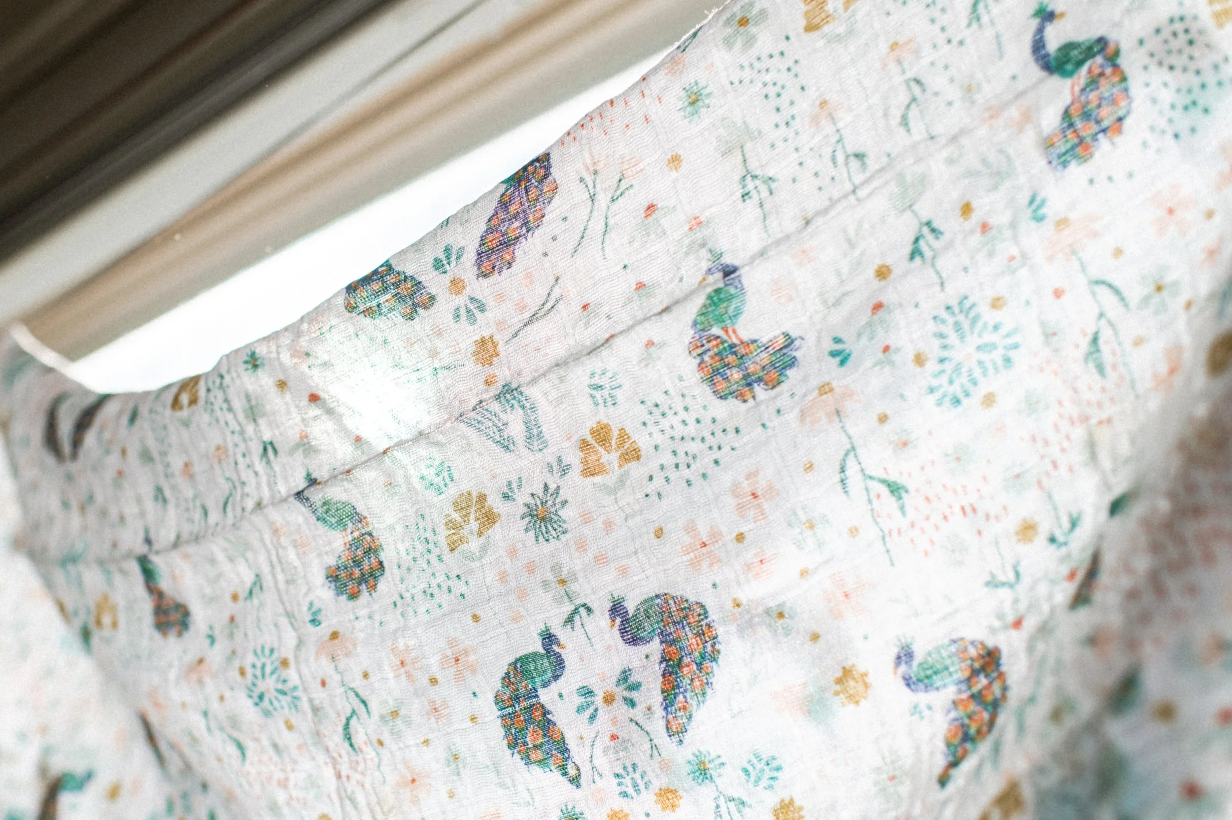 peacock organic cotton swaddle product photo that is hanging in window backlit