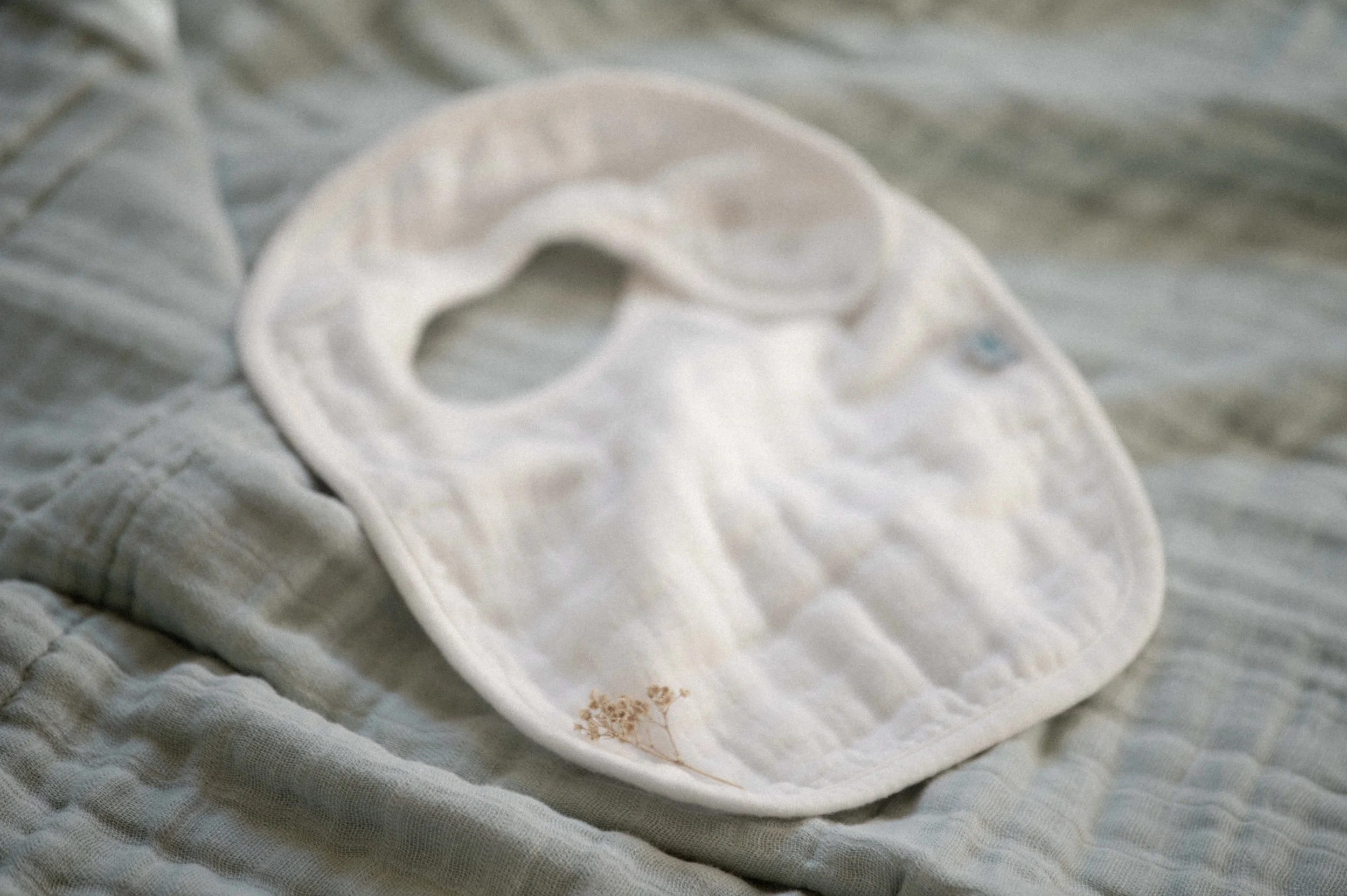 flat lay image of white bib on blue muslin organic cotton with dried florals