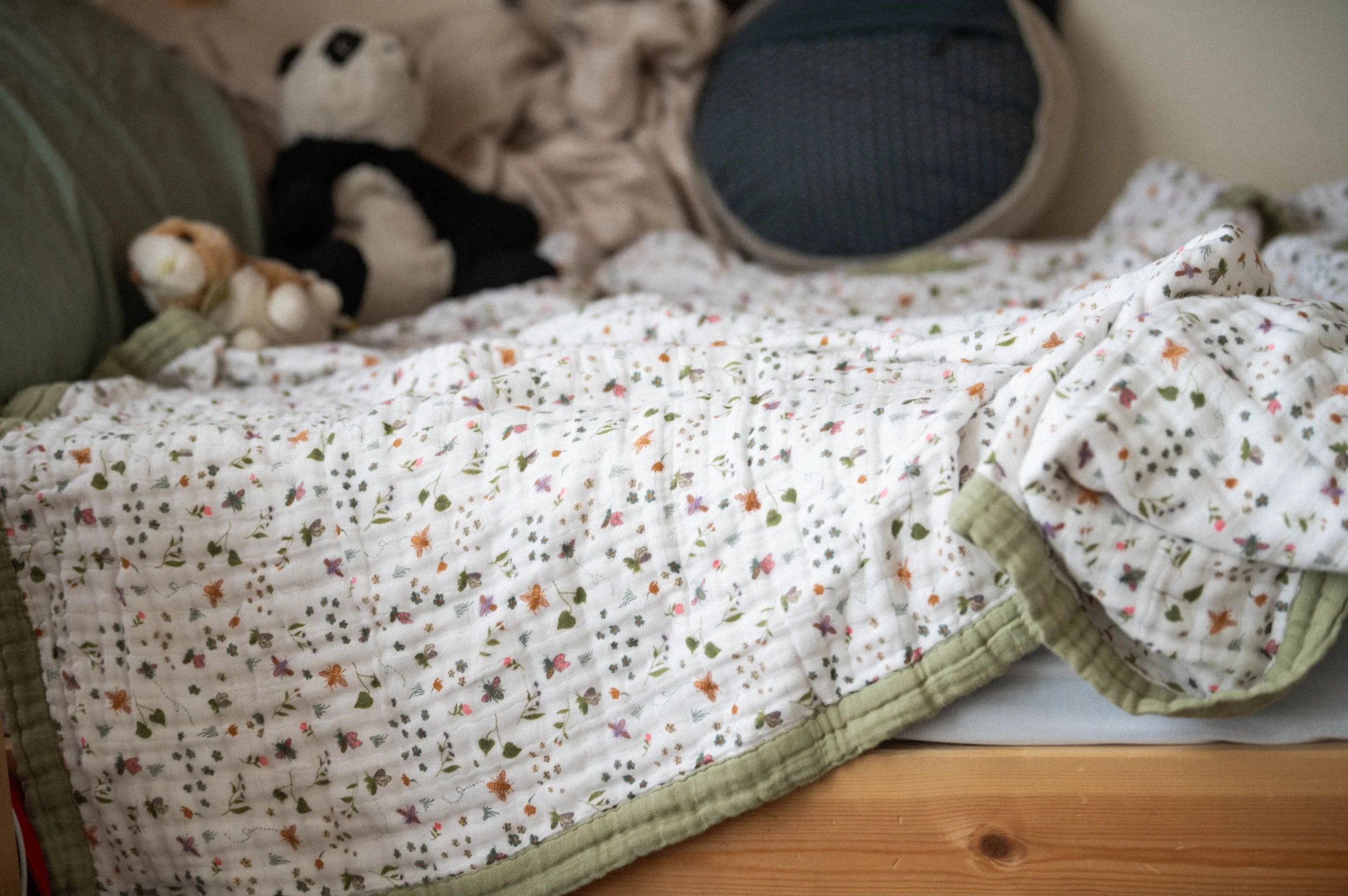 organic cotton floral blanket on bed with stuffed animals in background