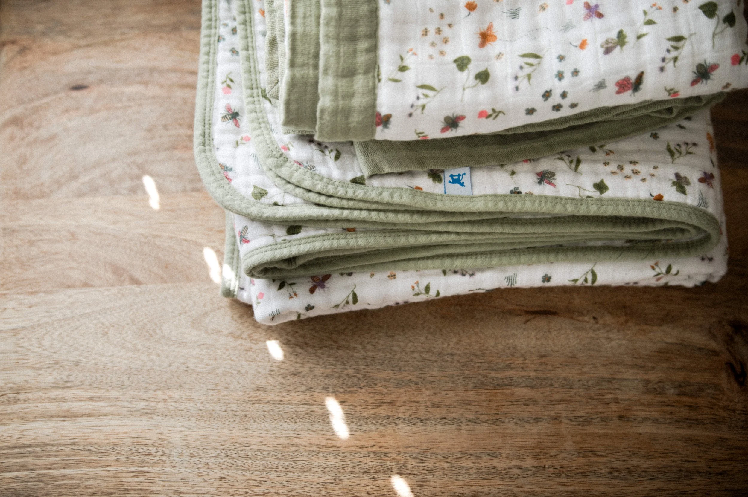 organic cotton floral swaddles with green edging on light wooden table with sunlight spots coming through