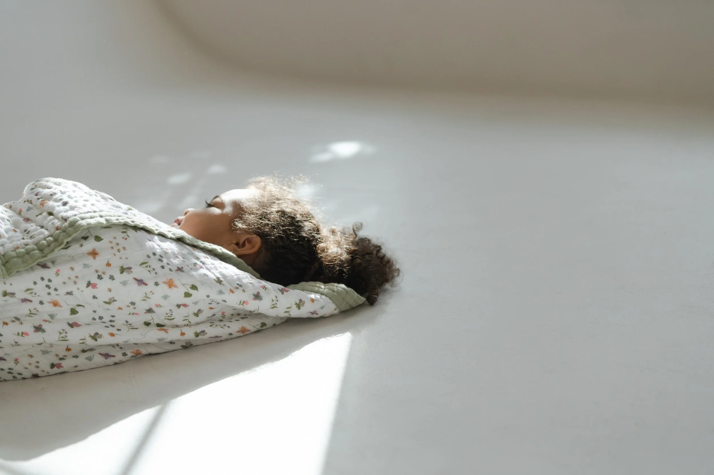 studio photography organic muslin blanket in window light with toddler snuggling in floral blanket