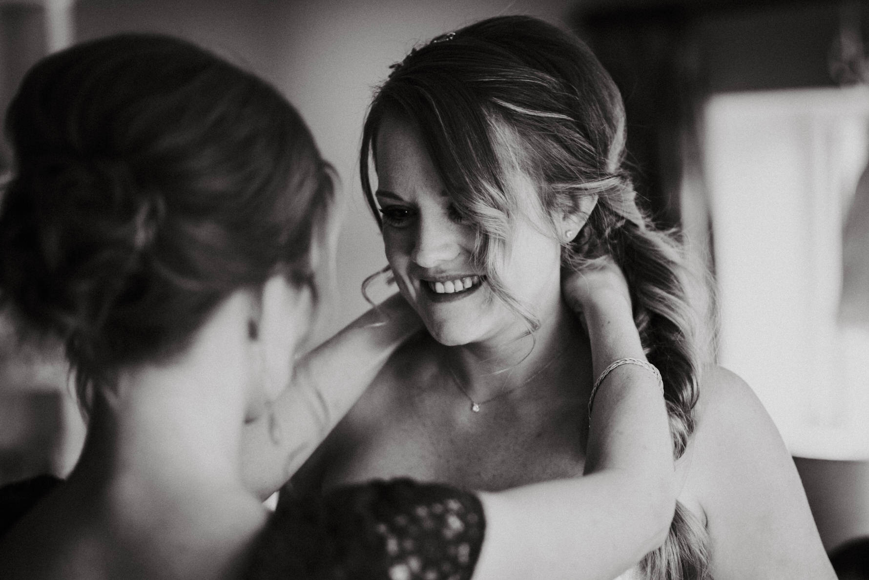 Documentary Wedding Photography - a bridesmaid helping the bride with her necklace