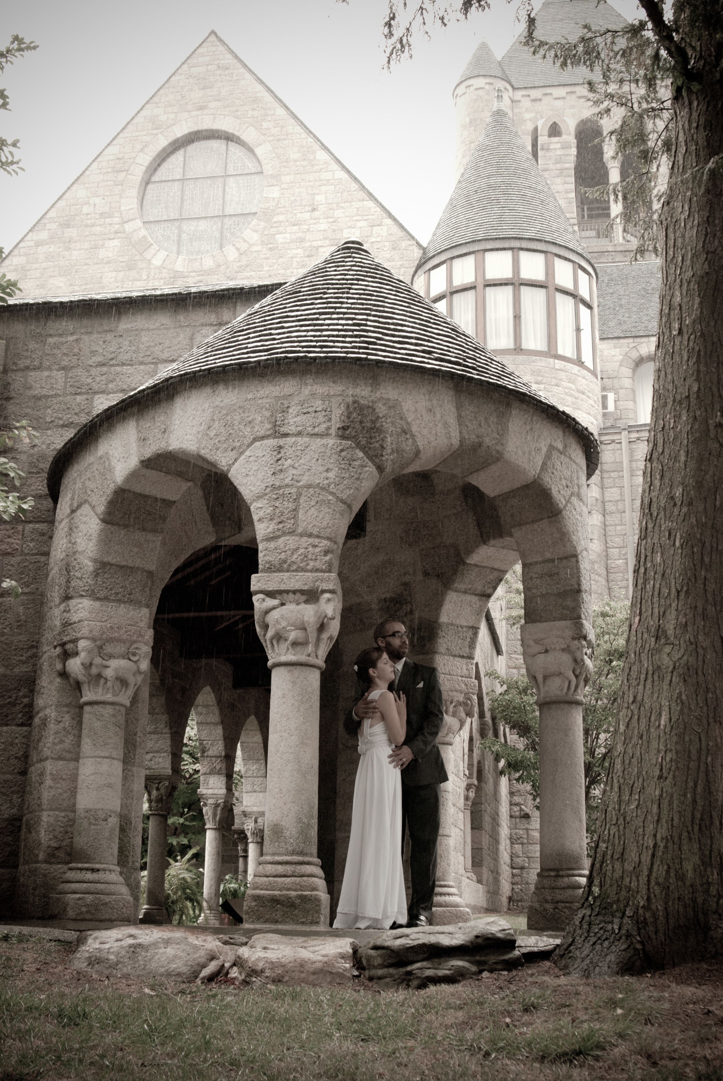 A sepia-toned image shows and bride and groom embracing in the turret entrance to Glencairn Museum's cloister garden.