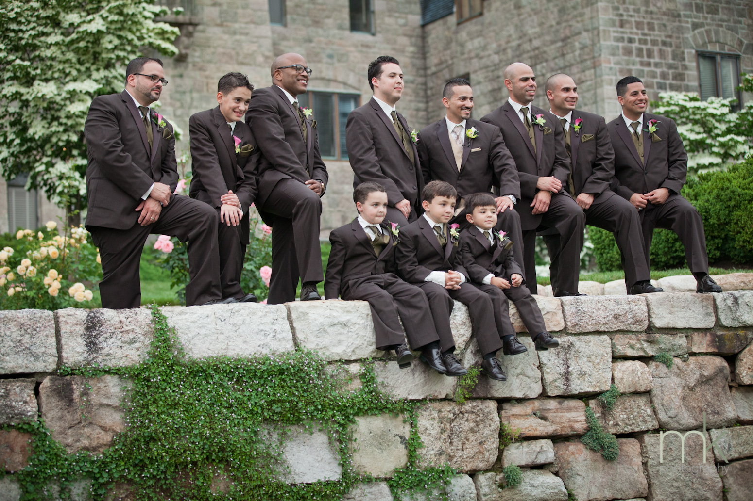 A groom surrounded by his groomsmen, pose on a stone wall outside Glencairn Museum.