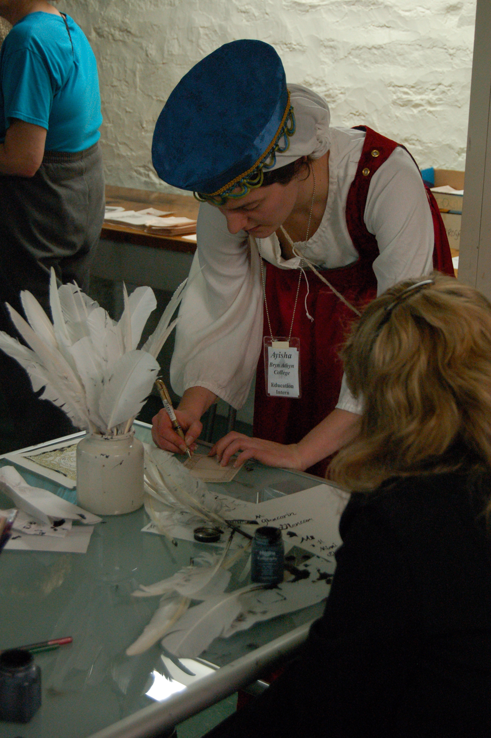 A volunteer helps a visitor try her hand at writing with a quill pen.