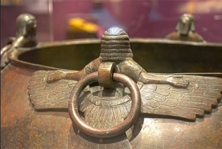 Figure 5: Cauldron from Tumulus MM, Gordion (MM 3), on loan to Penn Museum from the Museum of Anatolian Civilization, Ankara, Turkey, showing back of a bearded demon attachment, with lifting ring intact. Photograph by Ed Gyllenhaal, with permission of Penn Museum.