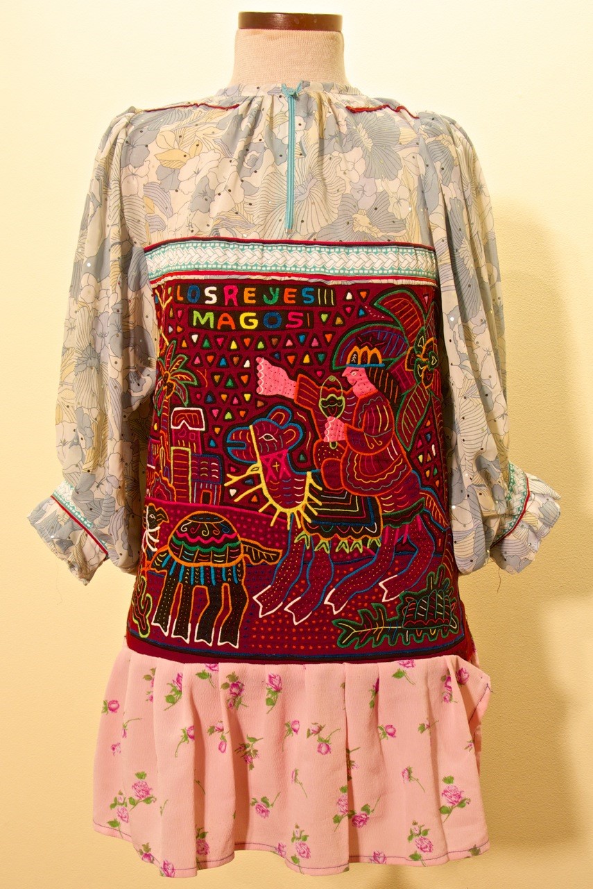 Figure 2: Blouse with Scenes from the Infancy of Christ. Two scenes from the Gospel of Matthew decorate the molas on this blouse. The front panel depicts the journey of the Holy Family during the Flight into Egypt. On the back (pictured here), one of the Wise Men, riding a camel and pointing to the Star of Bethlehem, carries a gift for the baby Jesus.