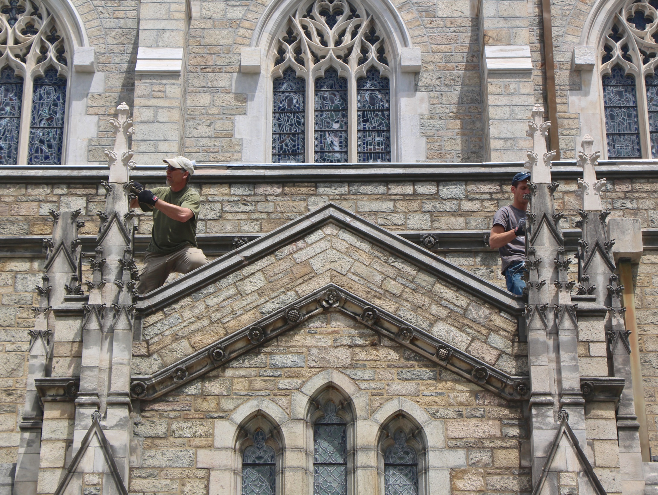 Figure 2: In this photo, three out of four new limestone finials have been set on original bases. Left: Jens Langlotz installs a finial and cleans excess mortar from the base. Right: Grayson Zuber does grouting and cleanup.