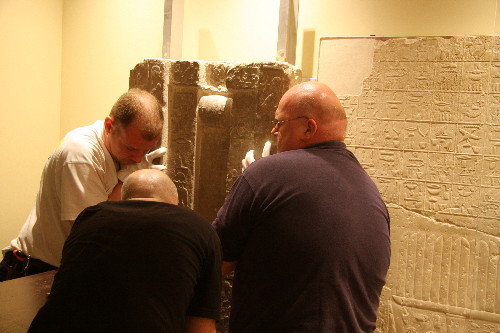 The installation team lifts the middle portion of Glencairn's spirit door into place beside a relief with Tep-em-ank's "menu list," which is on loan from the Louvre Museum.