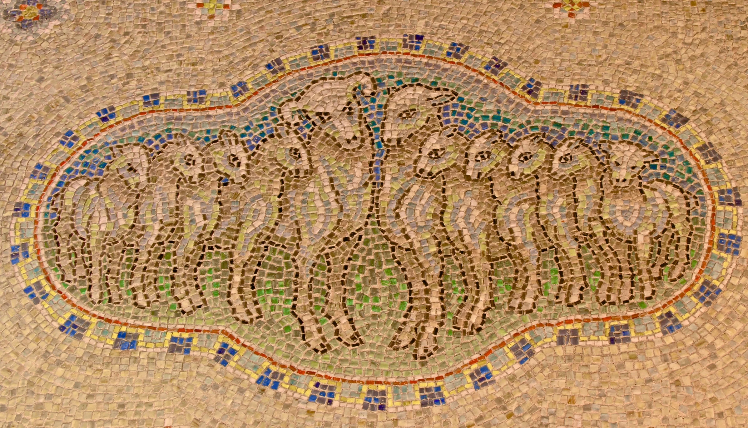 Figure 1: The wall above the elevator door on the first floor of Glencairn features a medallion in glass mosaic depicting the Pitcairn family as a ram, a ewe, and nine lambs. In addition to admiring medieval stained glass, Raymond Pitcairn was fascinated with the mosaics of Italy—especially those in the 5th and 6th century churches of Ravenna—and wanted to decorate his home with mosaics of a similar quality. Pitcairn’s craftsmen developed formulas for making their own glass mosaics in the Bryn Athyn glassworks.