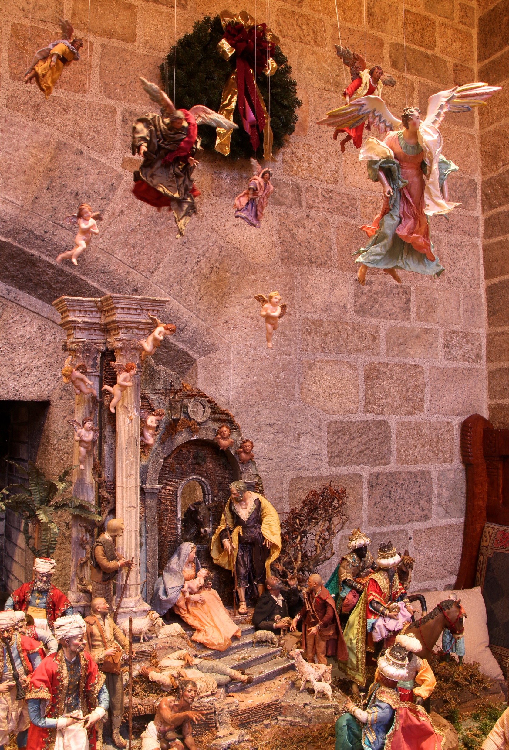 The Holy Family is positioned in the midst of Roman ruins, while a host of angels descends from heaven above. Shepherds visit with their sheep and wise men from the East arrive on horseback.