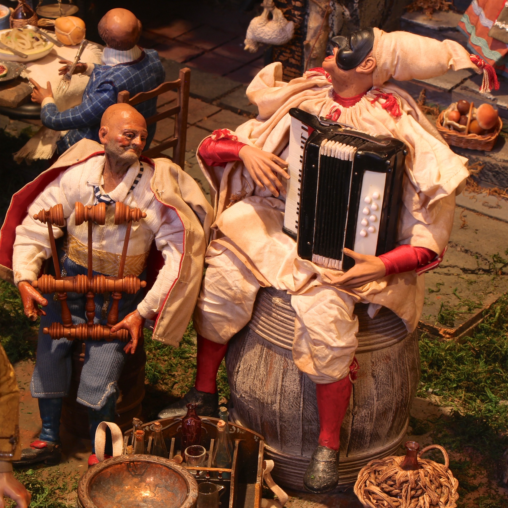 Figure 9: Two musicians at the tavern play Italian folk instruments. The triccheballacche (left) is a Neapolitan percussion instrument. Pulecenella, a stock character in Neapolitan puppetry who wears a mask, plays the organetto (right).