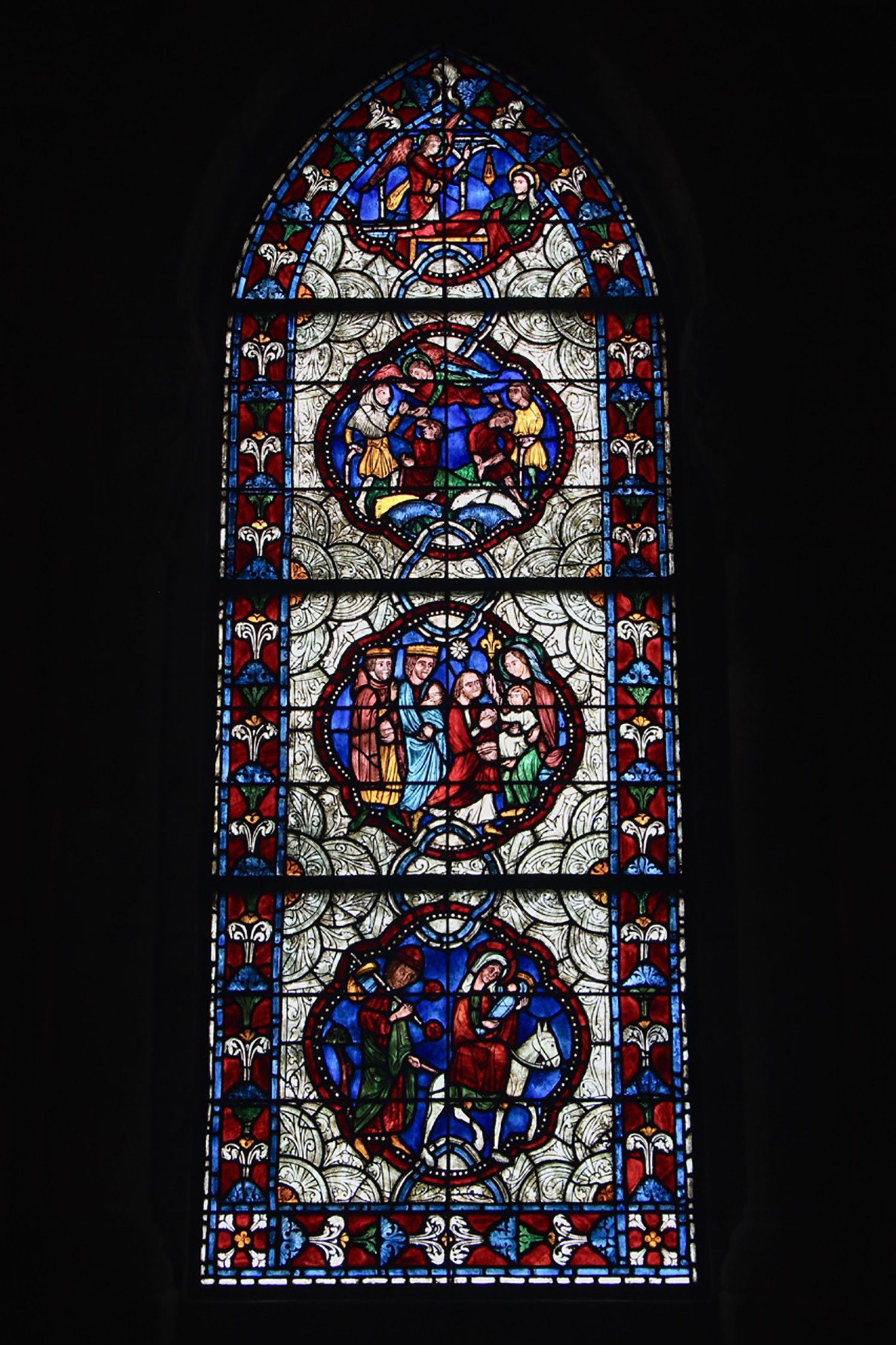 Figure 15: The two side walls of Glencairn’s chapel hold stained glass windows inside Gothic arches, both made in the Bryn Athyn glassworks. The south window shows scenes from the birth of Jesus Christ. The three complete medallions are reproductions of part of a thirteenth-century window in the nave of the church of Sainte-Radegonde in Poitiers, France. The scene at the top of the window is presumed to be an original design drawn up in Bryn Athyn’s stained glass studio.