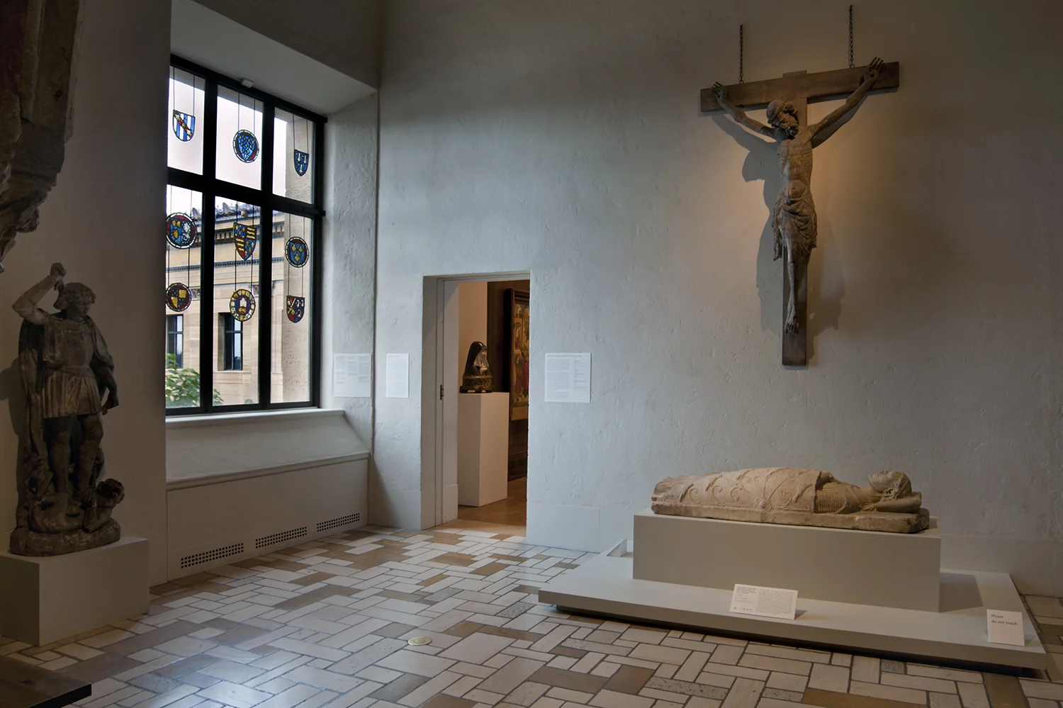 Figure 5: View of a gallery of French Gothic sculpture and English stained glass at the Philadelphia Museum of Art, featuring a Corpus of Christ of the late 13th or early 14th centuries and a Saint Michael Vanquishing the Devil of c. 1500, on long-term loan from Glencairn Museum, alongside the Philadelphia Museum of Art’s Tomb Effigy of a Recumbent Knight of c. 1230-40.