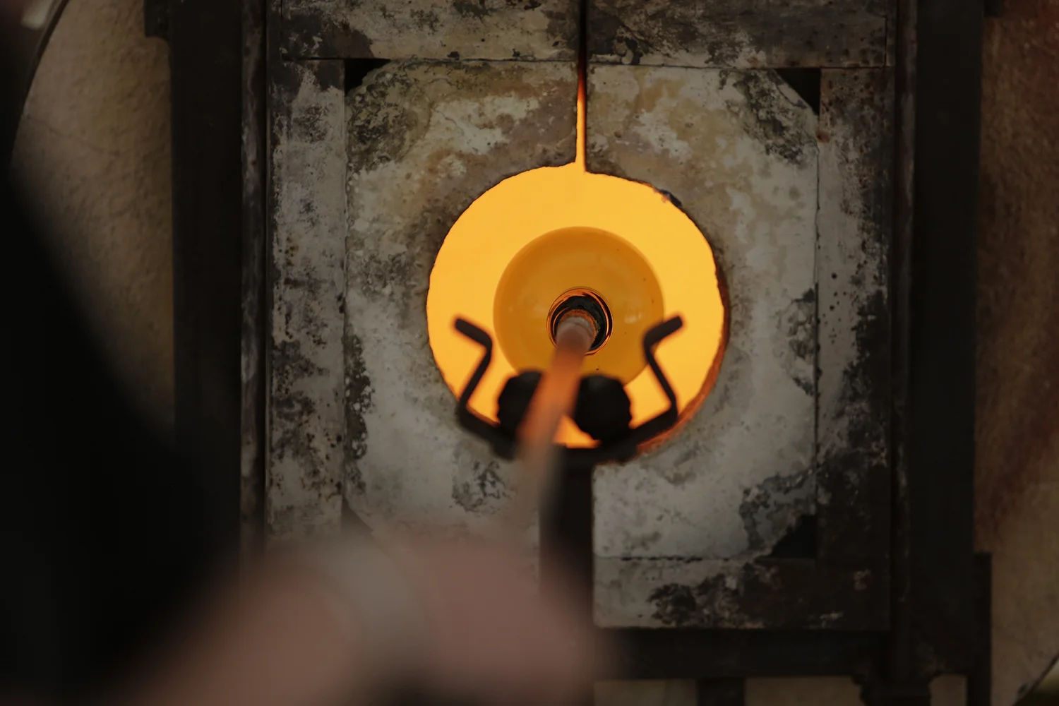 Figure 1: A gather of glass on the end of the blowpipe sits suspended in the small opening of the furnace. This opening is sometimes called the “glory hole.”
