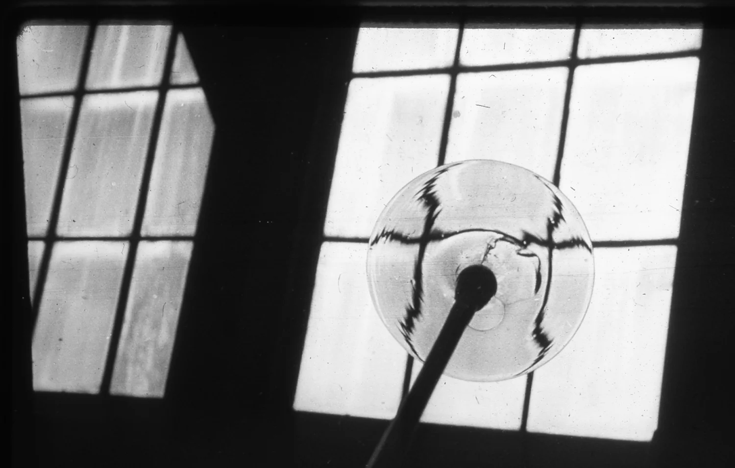 Figure 9: In this archival photograph, a rondel of glass is displayed against the light of a window in the Bryn Athyn glassworks.