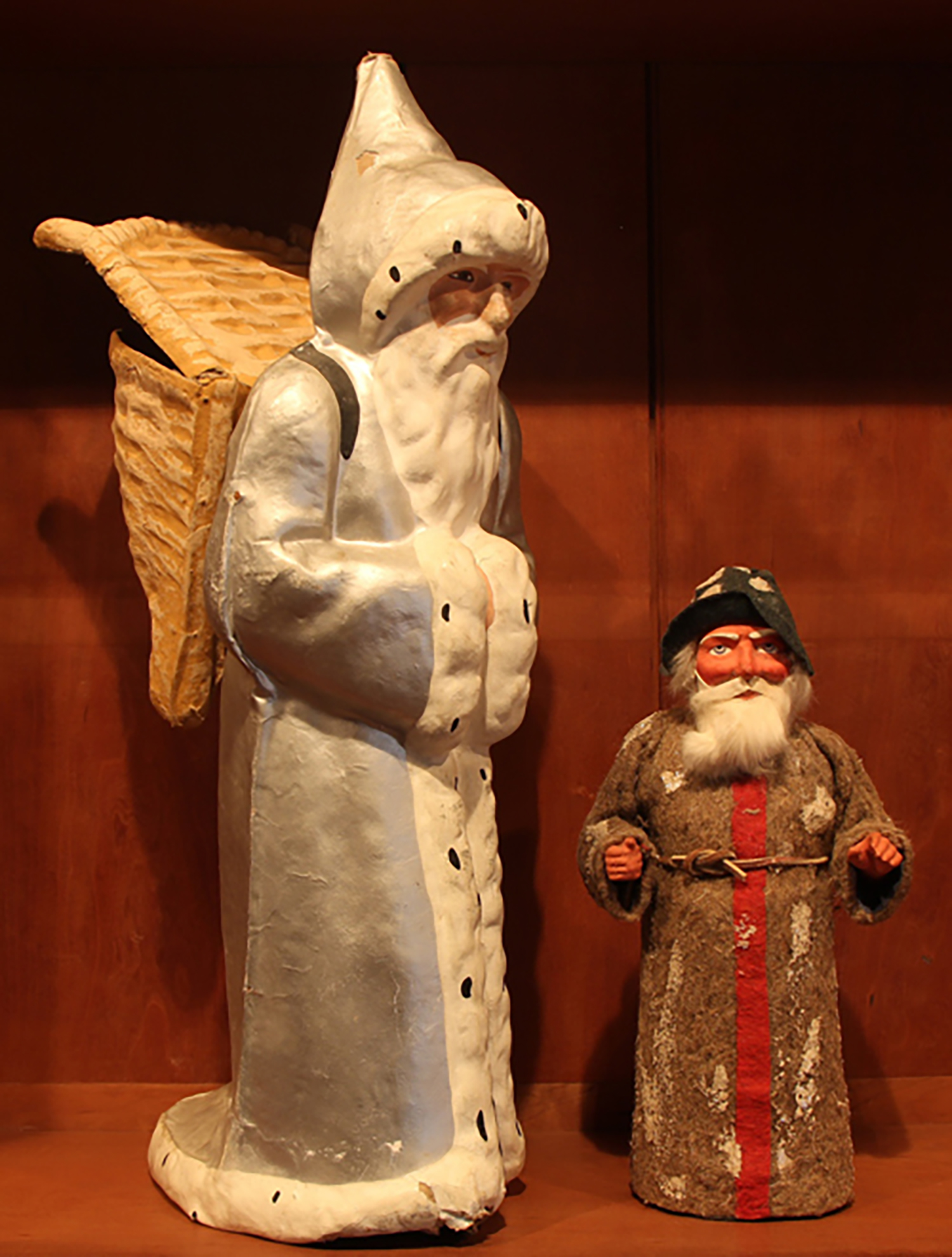 Figure 5: Left: Père Noël is the French equivalent of the American Santa Claus. He wears a long, hooded robe edged with white fur, and carries presents in a wicker basket like the ones traditionally used by grape harvesters. This papier-mâché figure of Père Noël, made in France around 1920, served as a candy container. Right: This St. Nicholas-shaped candy container, made in Germany around 1910, separates at the base and conceals a cylinder that held candy.