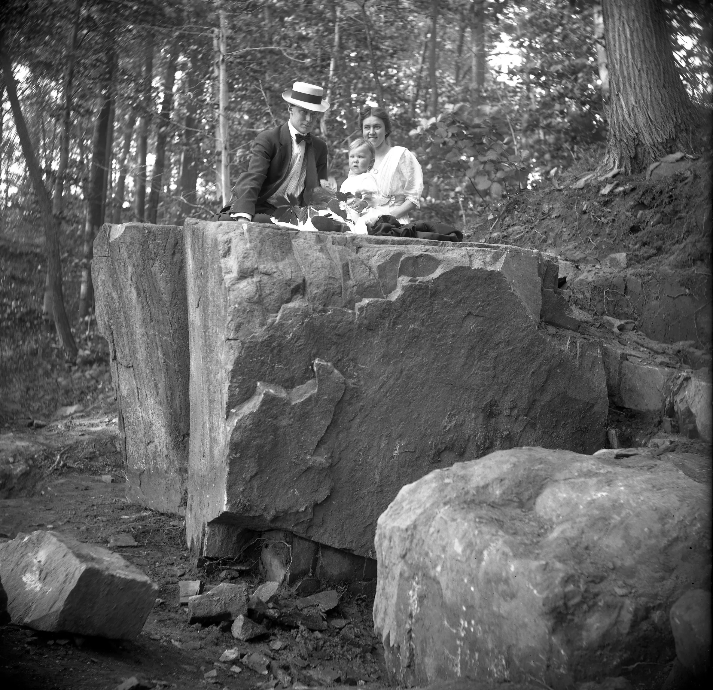 Figure 2: Raymond and Mildred Pitcairn pose on the cornerstone in the woods with their son Nathan.
