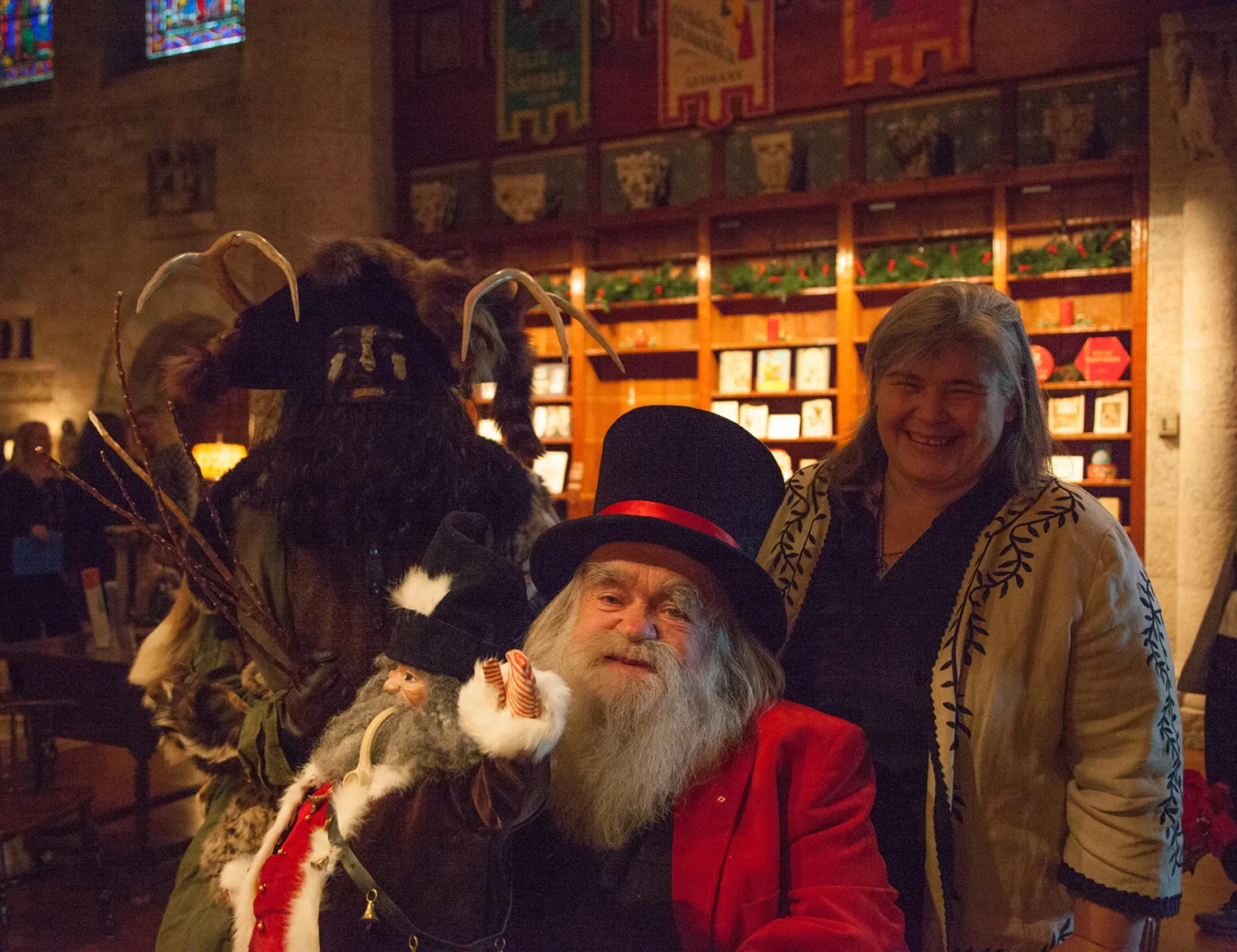 Figure 6: Nancy Schnarr-Bruell, from Bryn Athyn, Pennsylvania, poses with “Belsnickel” (aka Patrick Donmoyer, director of the Pennsylvania German Cultural Heritage Center) and “Santa Jr.” (aka Jim Morrison, founder/curator of the National Christmas Center). Santa Jr. is holding a Belsnickel doll crafted by Schnarr-Bruell. Photo taken in Glencairn’s Great Hall in 2016.