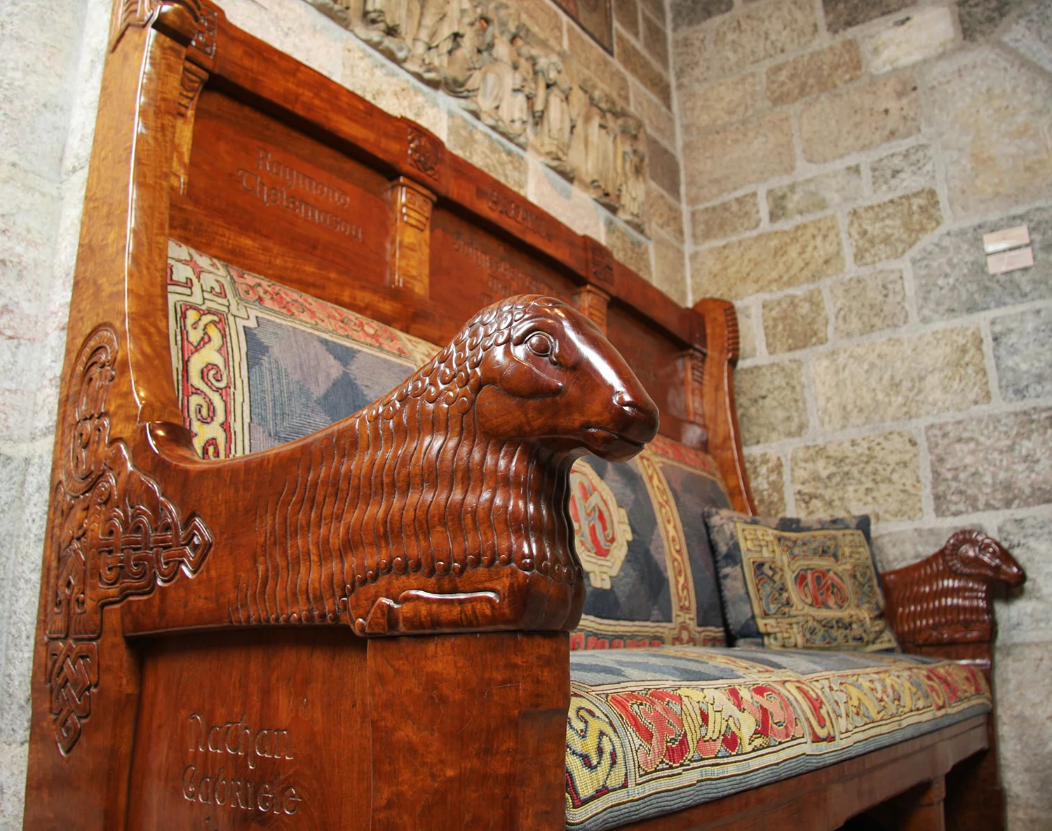 Figure 6: Glencairn’s Great Hall features a large fireplace flanked on either side by carved teakwood benches. Complex interlace patterns seen on the side of the bench were inspired by the Book of Kells, a ninth-century Irish Gospel book. Carved rams, ewes, and lambs signify the importance of family.
